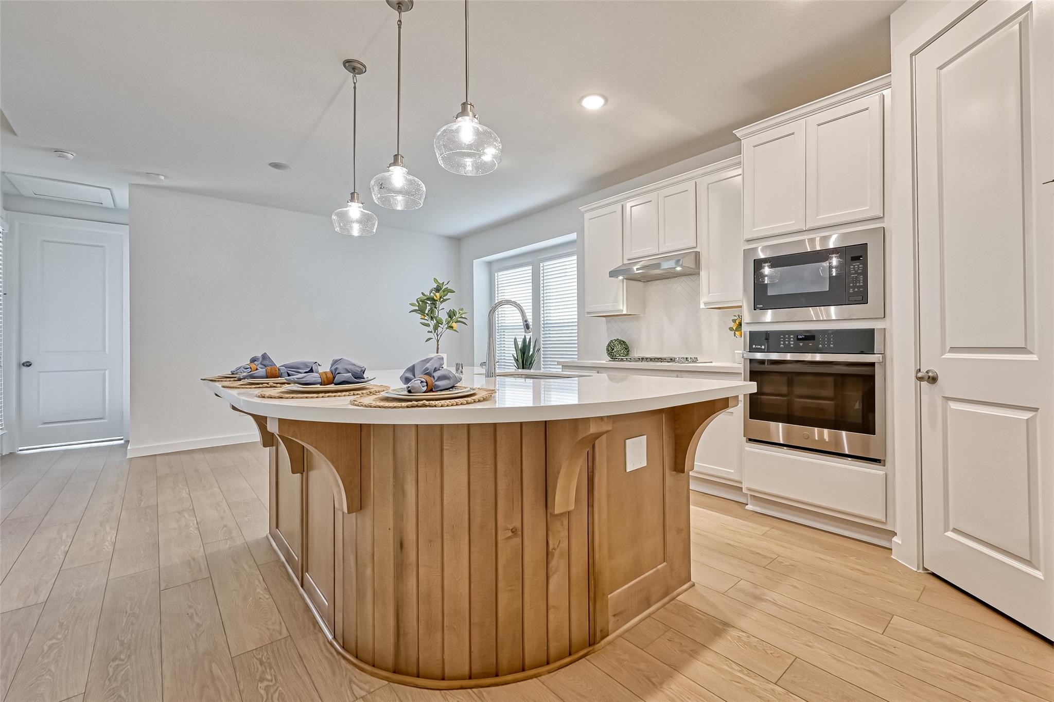 Modern kitchen with a curved wood island, white cabinetry, and stainless steel appliances.