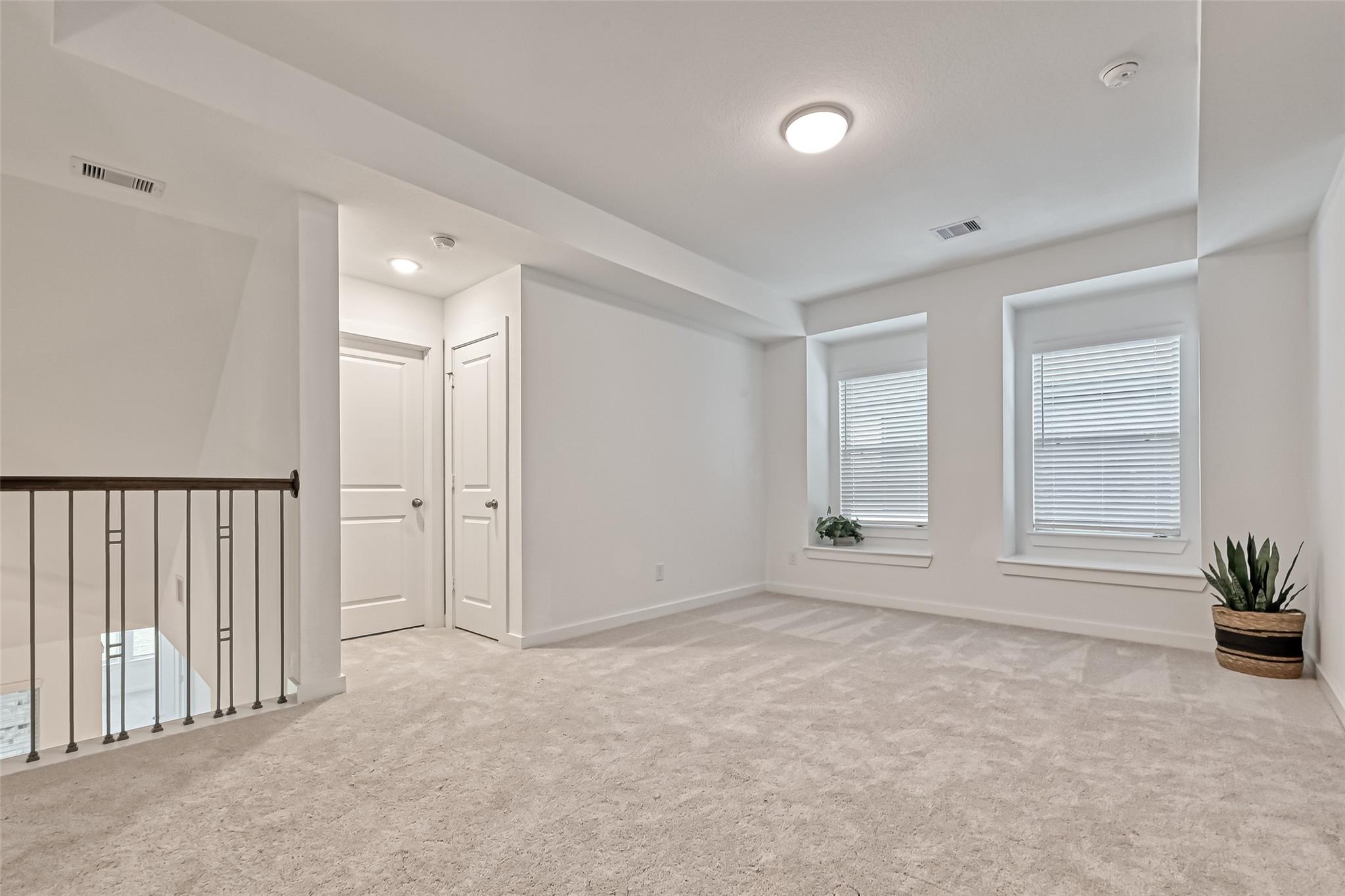 Upstairs loft with beige carpet, two shuttered windows, and a black metal stair railing.