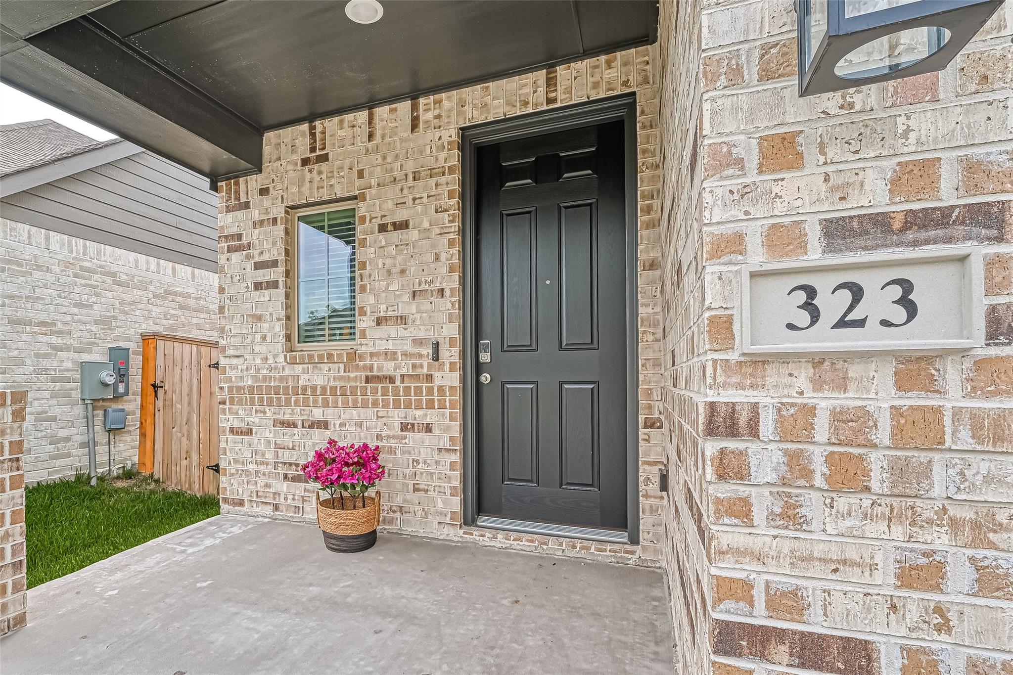 Covered brick entry with a black front door, house number 323, and potted pink flowers.