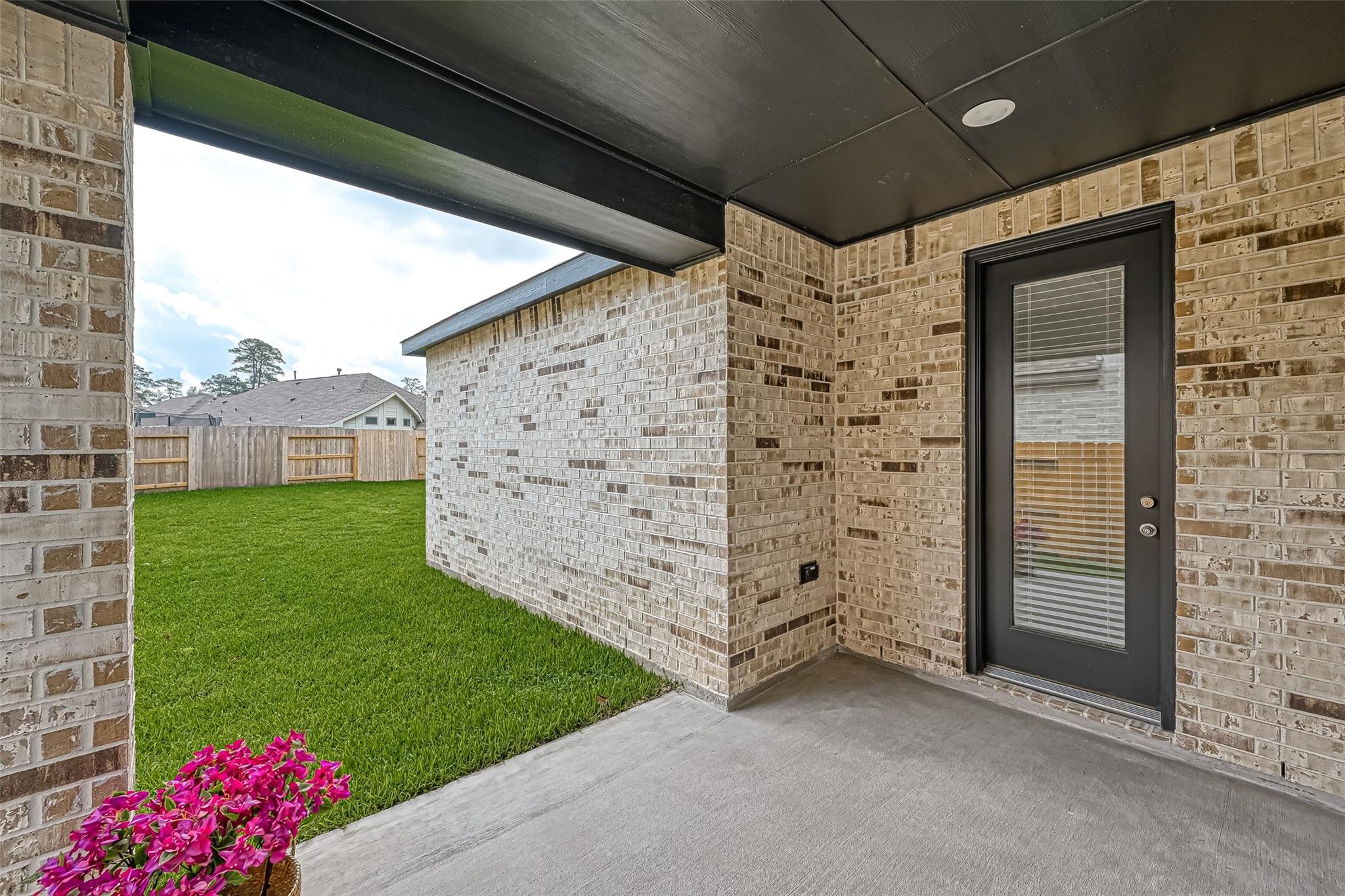 Covered brick patio with a dark back door overlooking a fenced lawn.