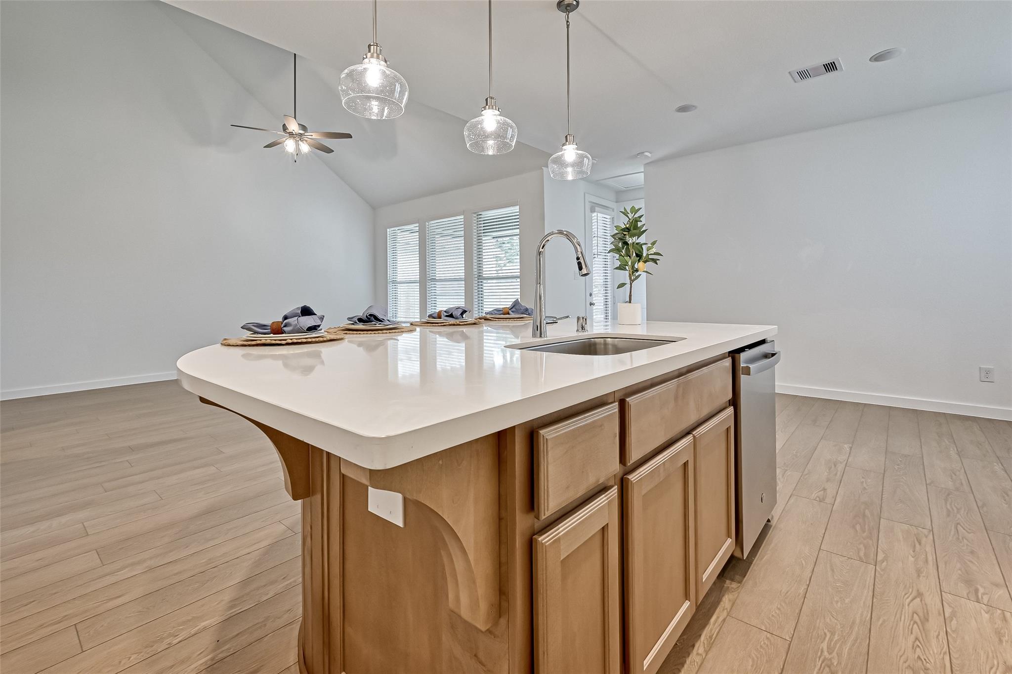 Bright kitchen with a large white island, integrated sink, pendant lights, and vaulted ceiling.