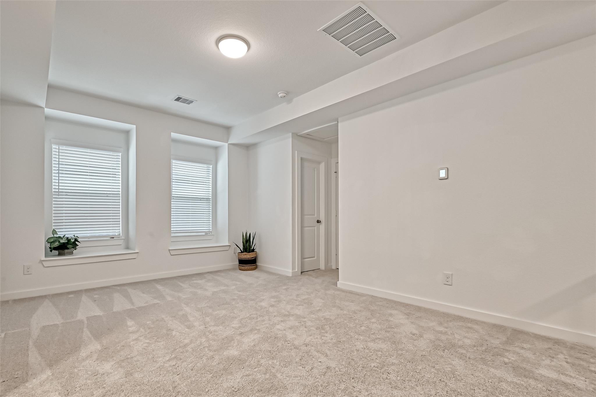 Empty carpeted bedroom with two recessed windows and white blinds.