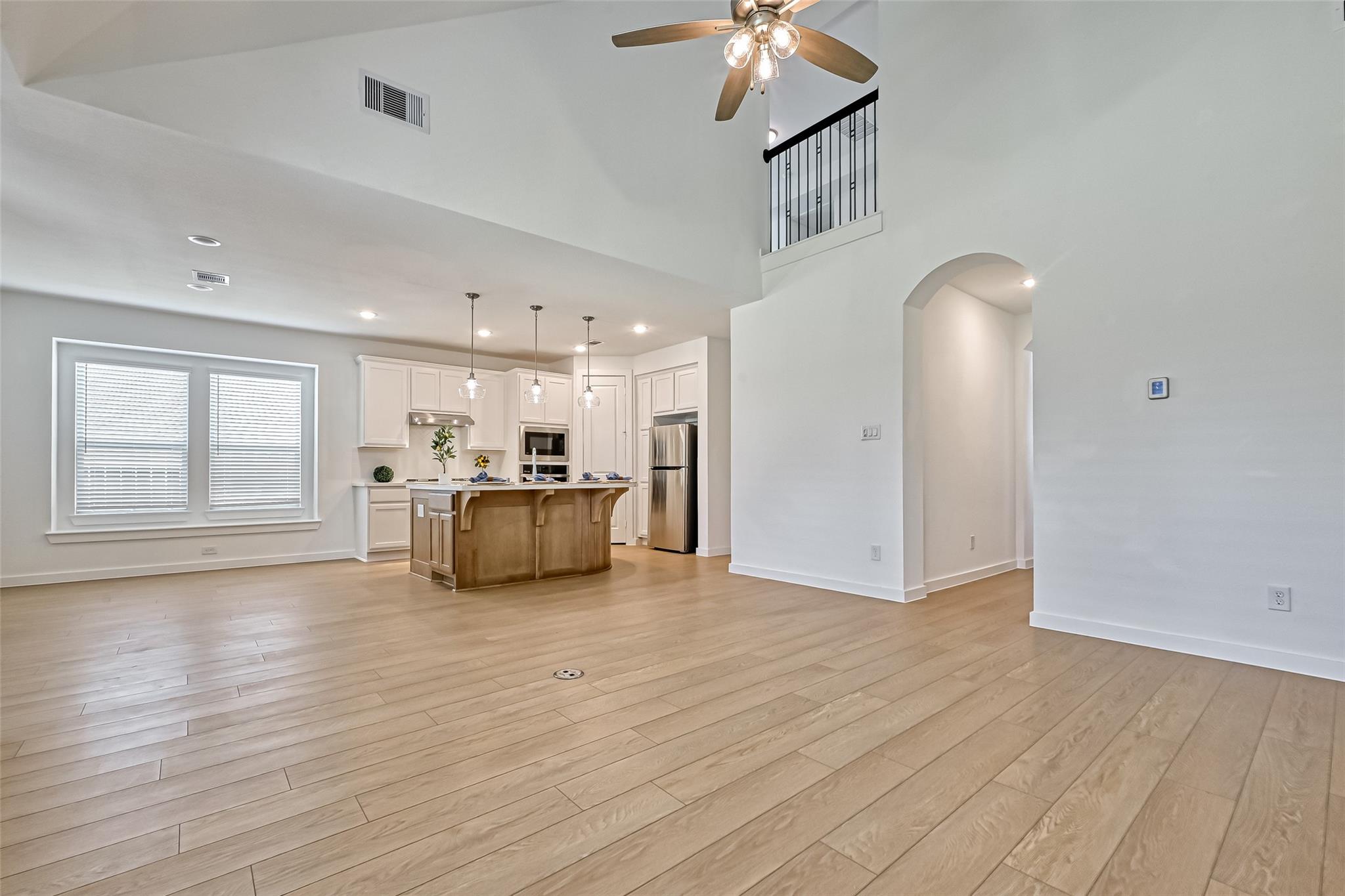 Open-plan kitchen with a wood-front island, stainless steel appliances, and a high ceiling with an upper railing.
