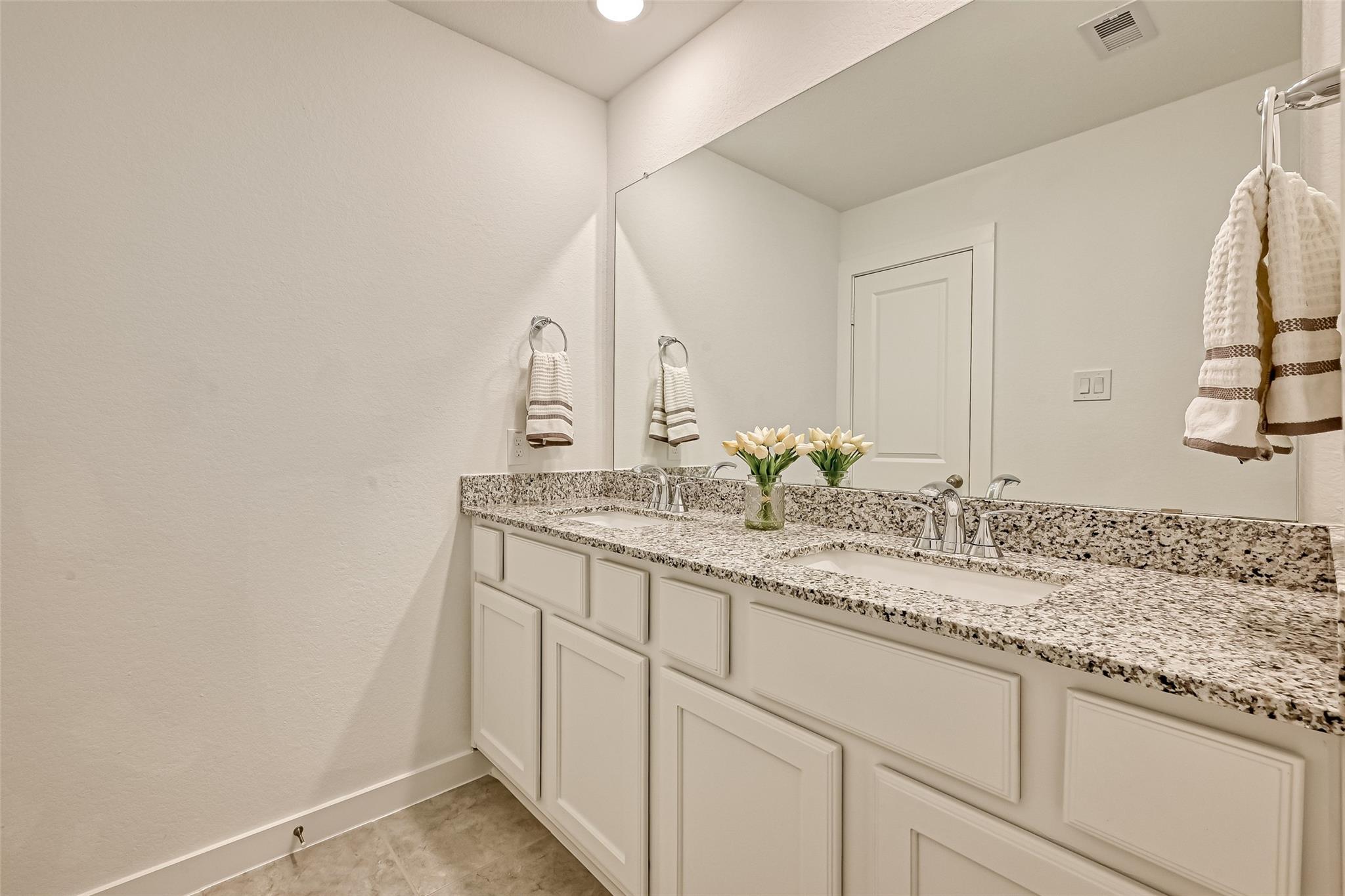 Bathroom with a double-sink granite vanity, large mirror, and white cabinetry.