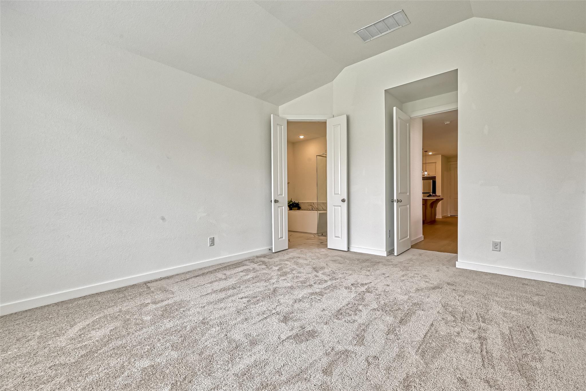 Empty carpeted bedroom with open doors to an ensuite bathroom and hallway.