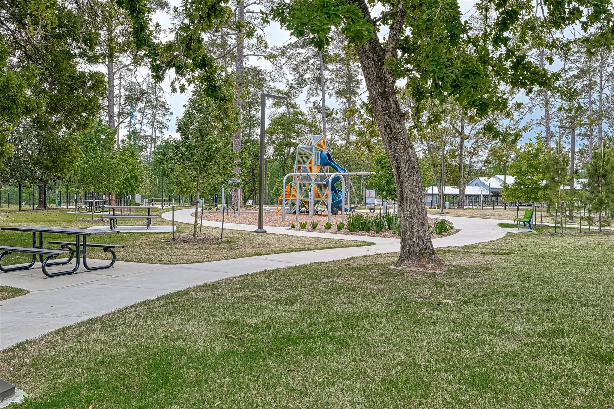 Community park with a colorful playground, picnic tables, and curving walking paths beneath mature trees.