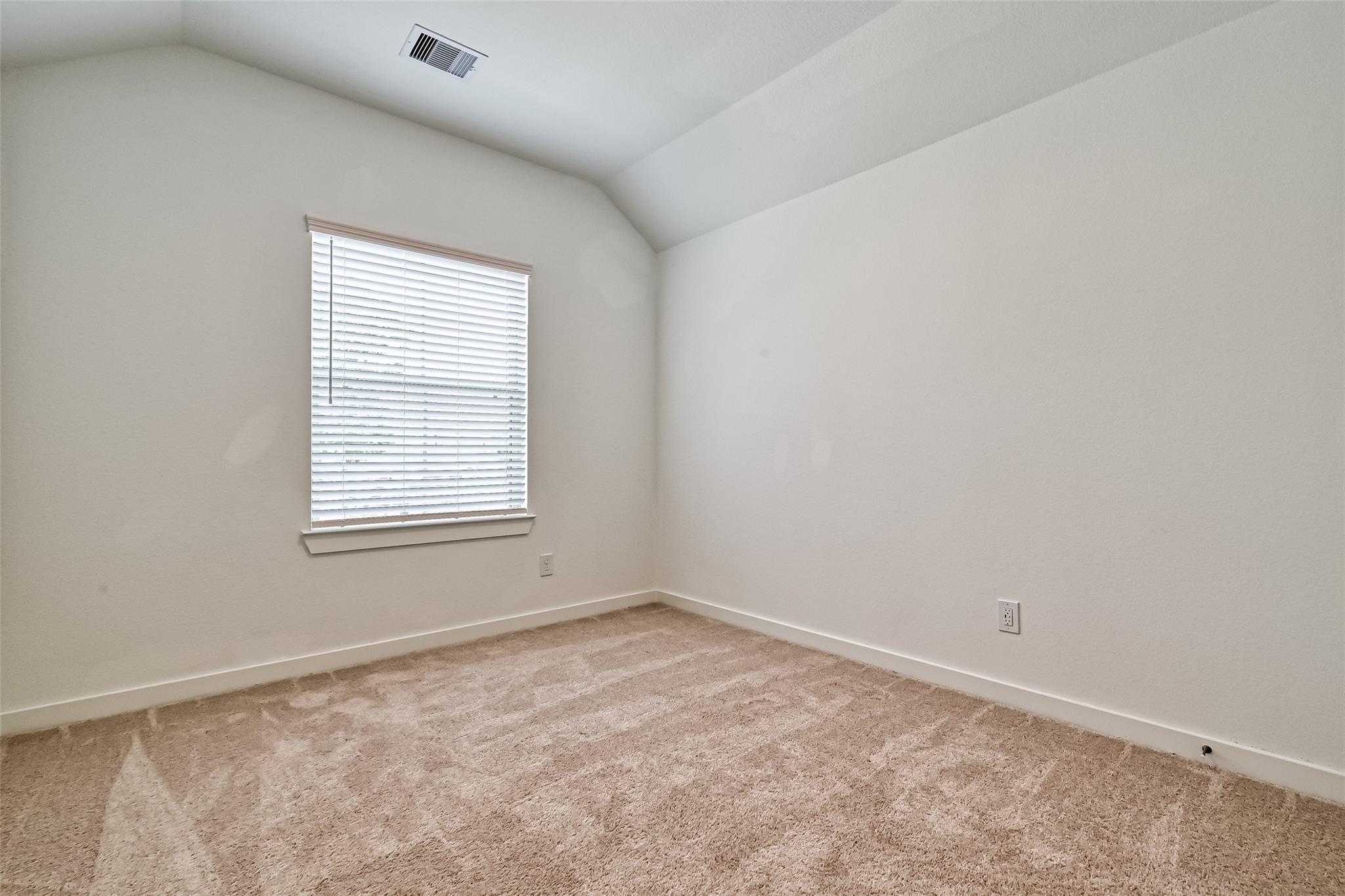 Empty bedroom with beige carpet, vaulted ceiling, and a window with white blinds.