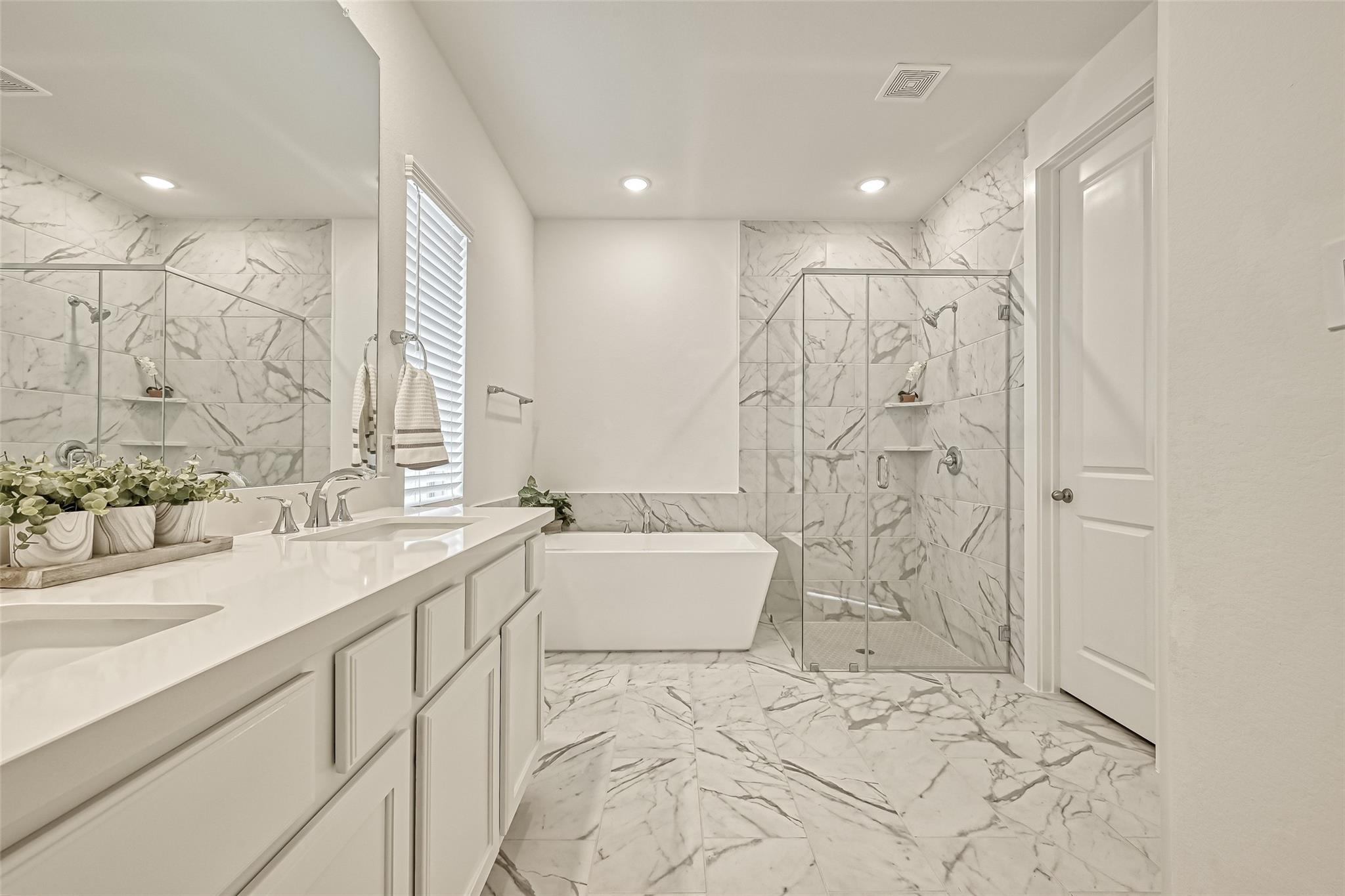 Bright bathroom with marble-look tile, a freestanding tub, and a glass-enclosed shower.