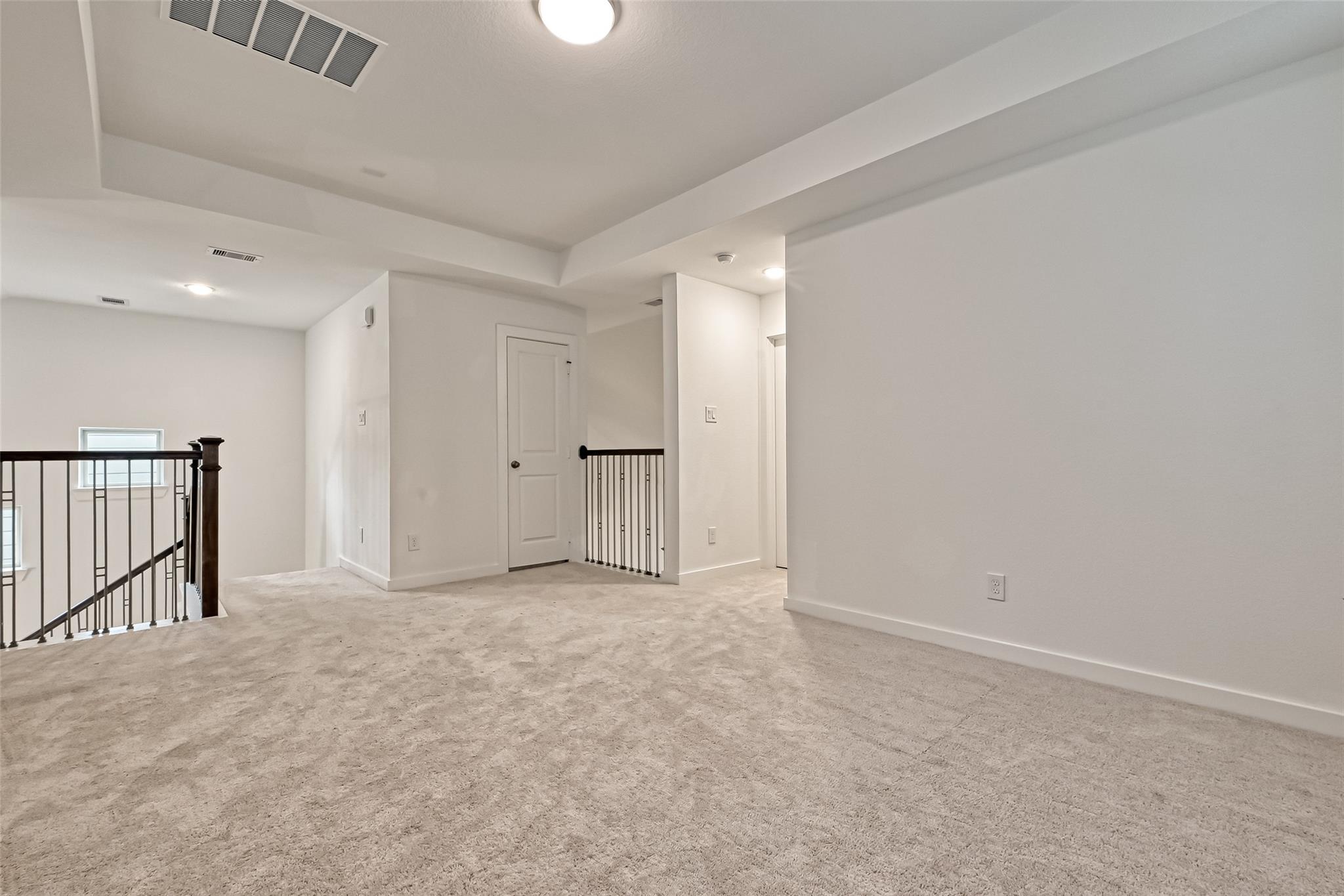 Carpeted upper landing with a tray ceiling and dark railings around the stairwell.