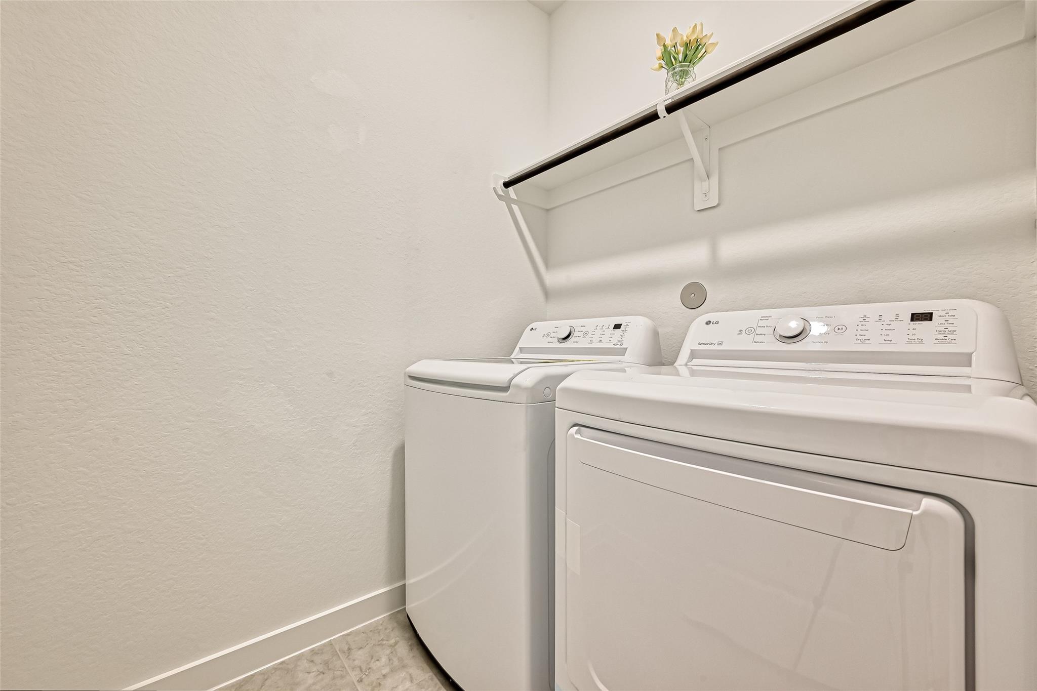 Laundry room with white washer and dryer beneath a wall shelf and hanging rod.