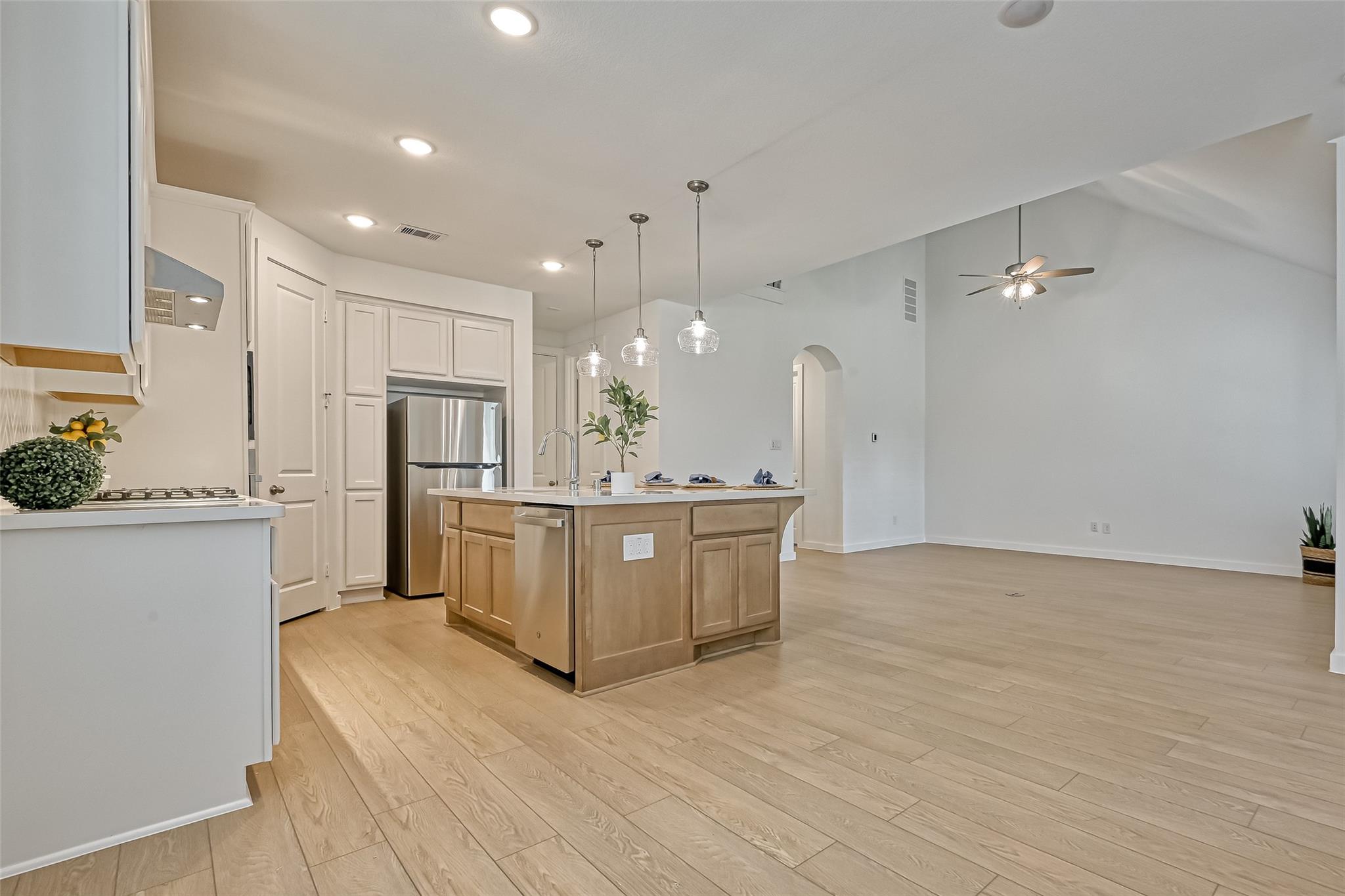 Open kitchen with a wood-toned island, stainless steel appliances, and glass pendant lights.