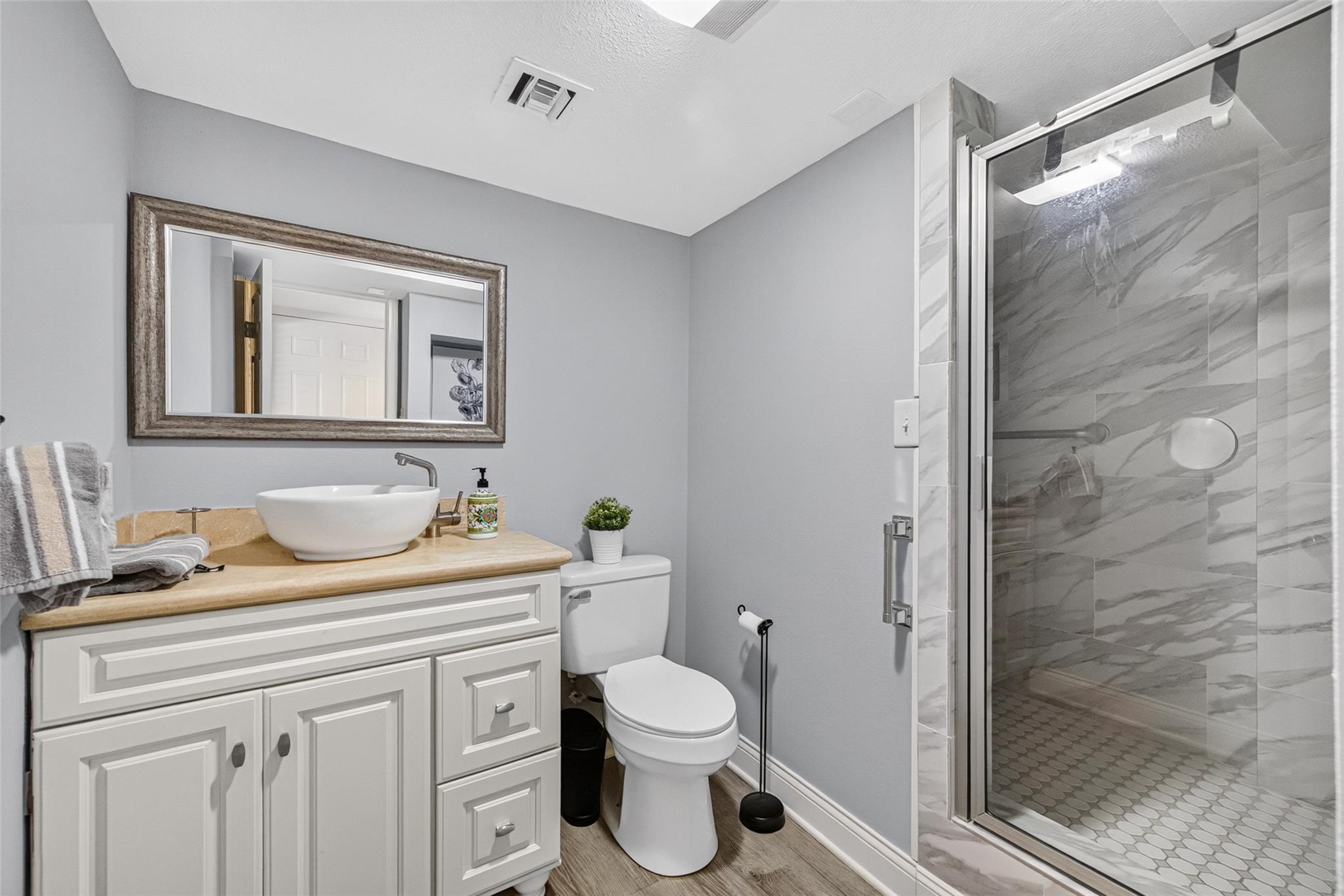 Bathroom with a vessel sink vanity and glass-enclosed marble-look tile shower.