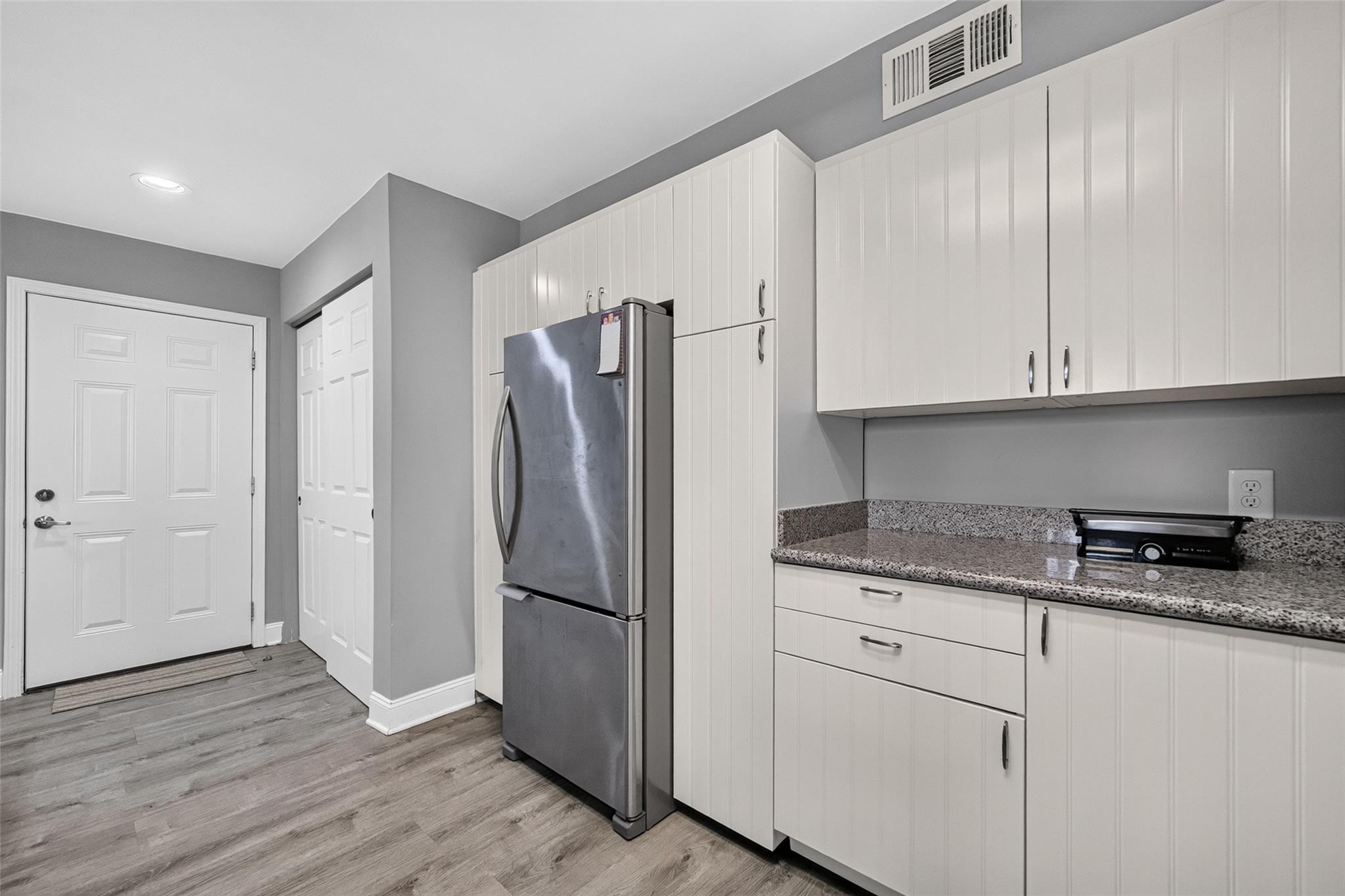 Kitchen with white cabinets, granite counters, stainless steel refrigerator, and gray wood-look flooring.