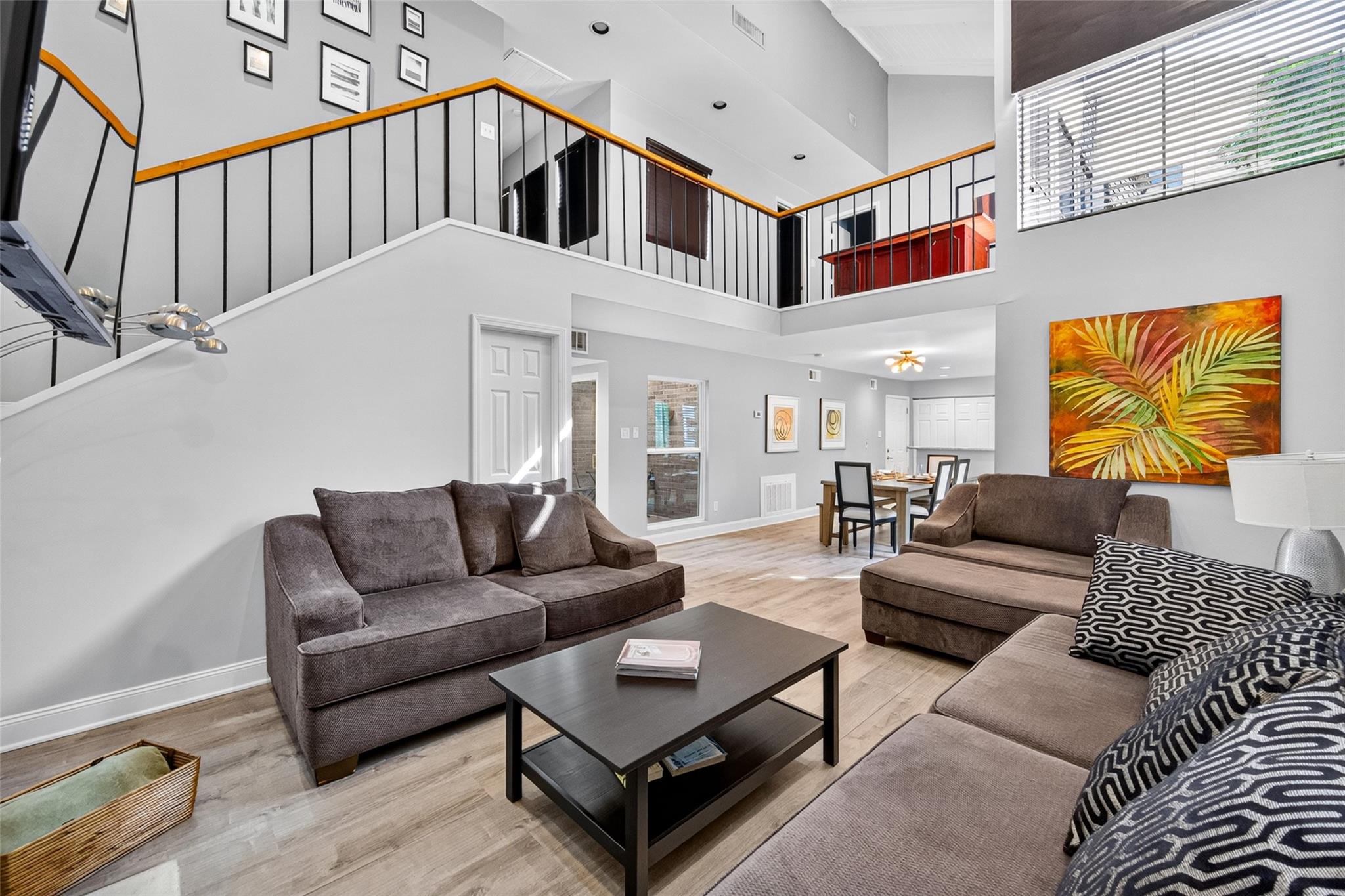 Two-story living room with brown sofas, open mezzanine, and dining area.