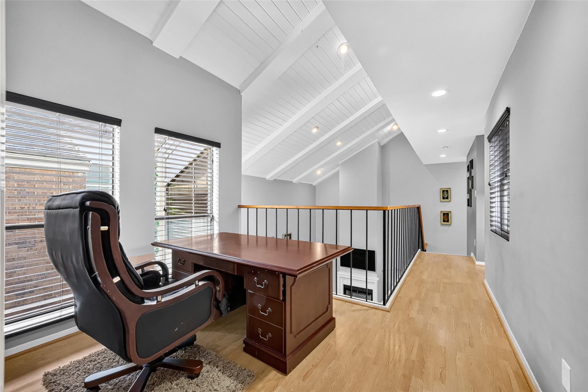 Upstairs office with a wood desk, leather chair, vaulted beamed ceiling, and railing overlooking the lower level.