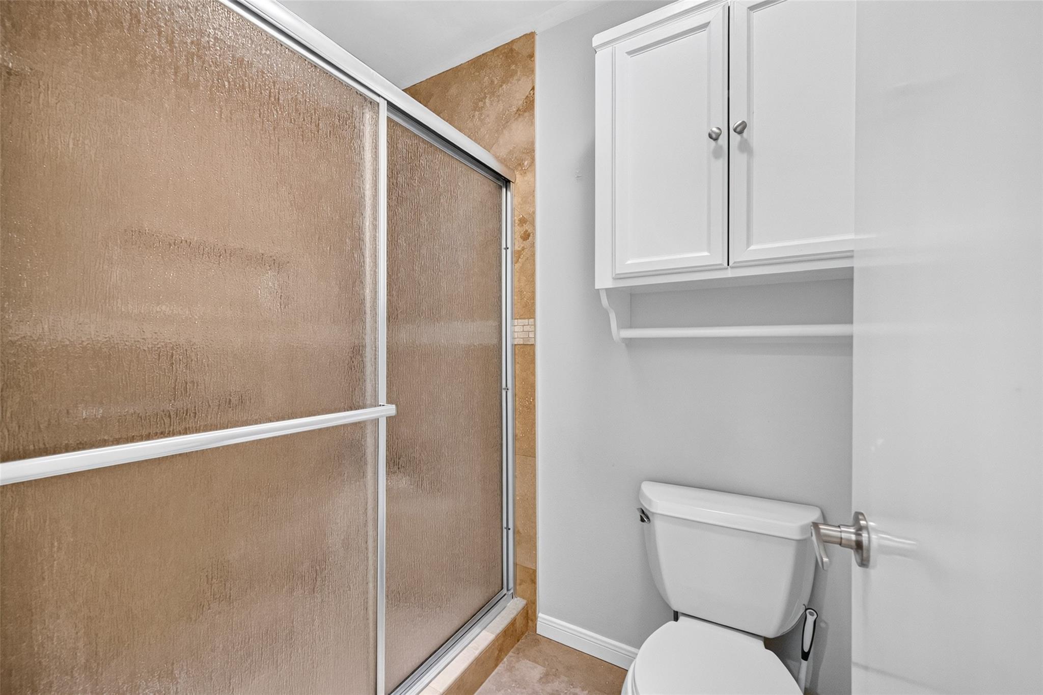Bathroom with a tan sliding shower enclosure, white toilet, and wall cabinet.
