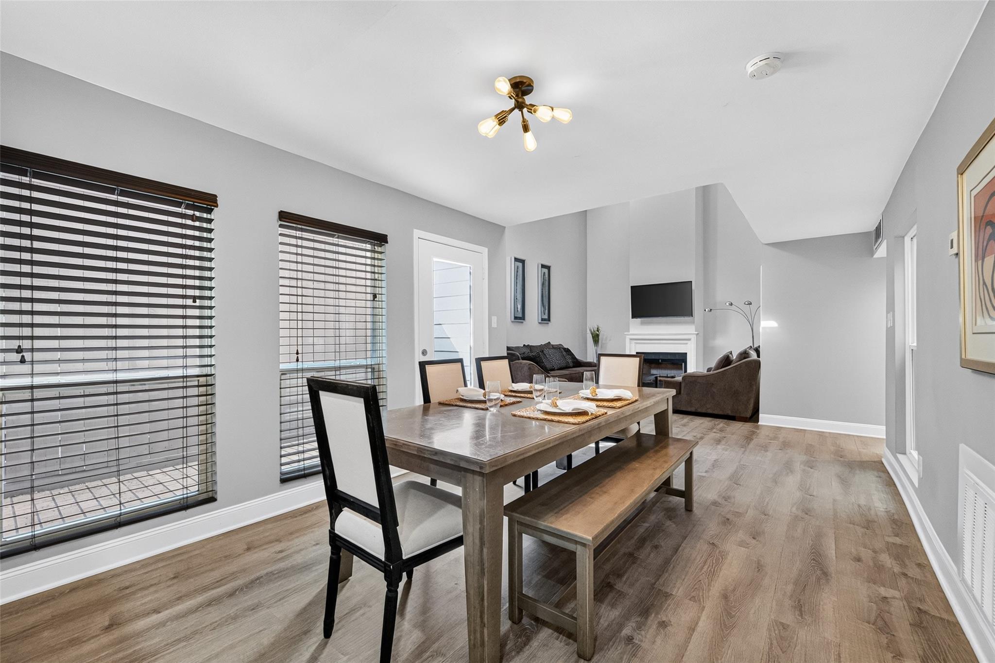 Dining area with a wood table and bench opening into a living room with a fireplace.