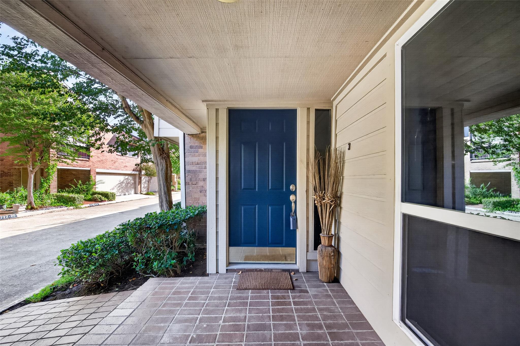 Covered townhouse entry with a blue front door, tiled porch, and decorative vase.