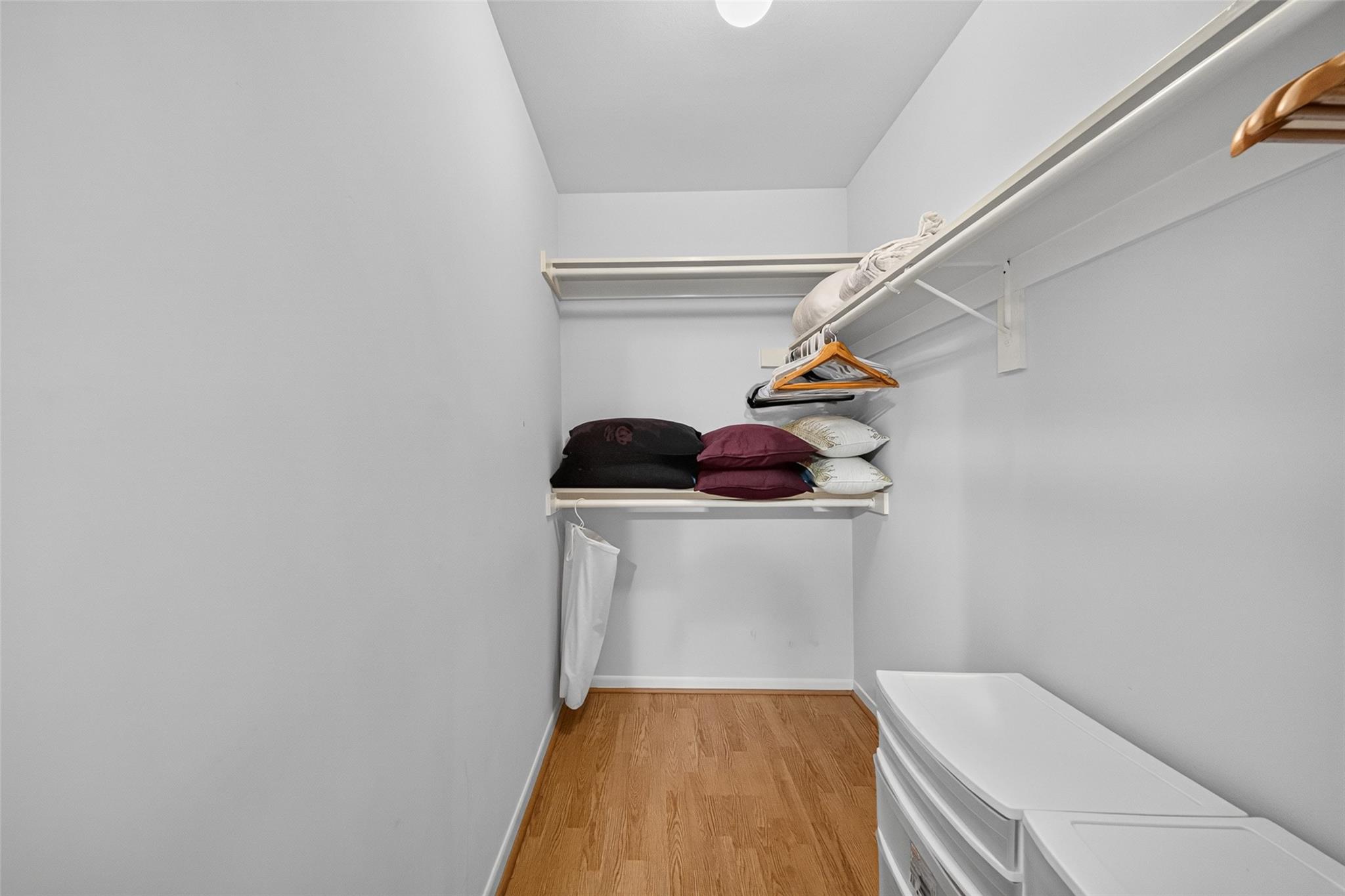 Walk-in closet with built-in shelving, pillows, hangers, and white storage drawers.