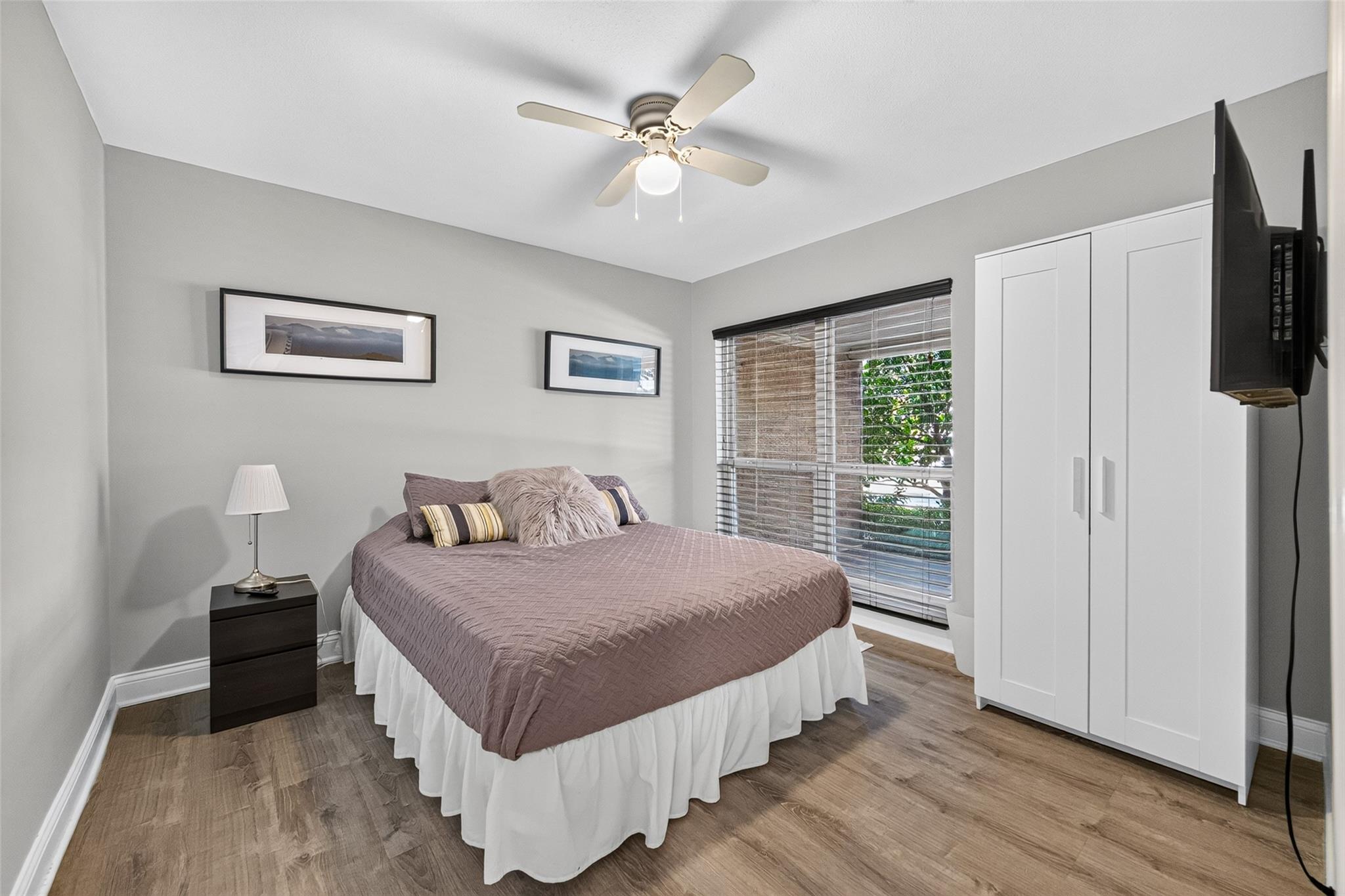 Bedroom with a mauve quilted bed, white wardrobe, and window overlooking greenery.