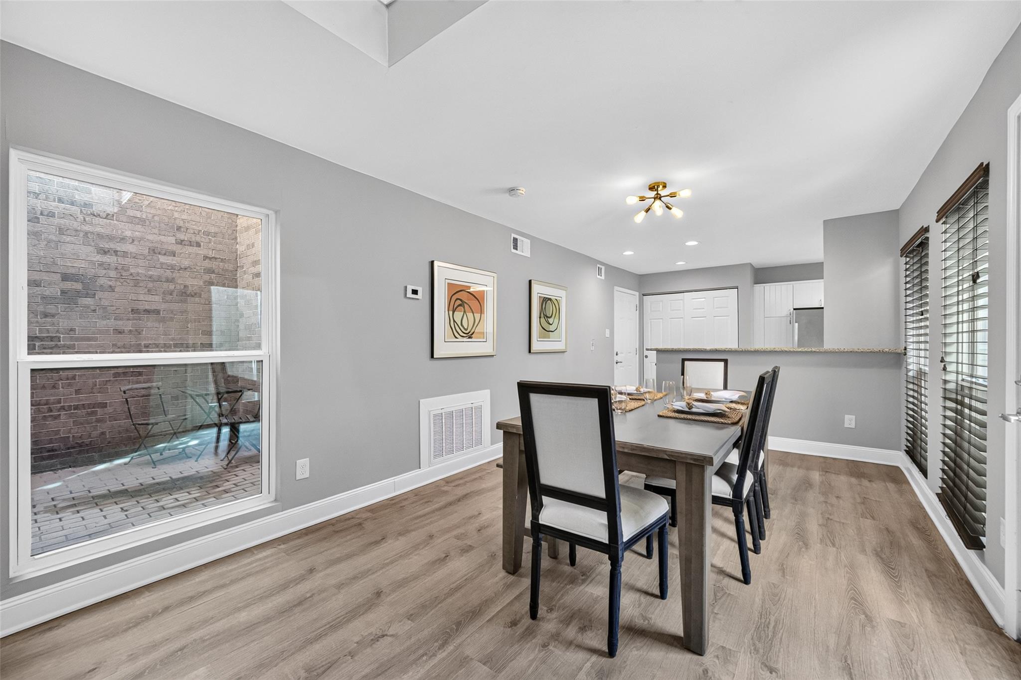 Dining area with a dark wood table beside a large window overlooking a brick-walled patio.