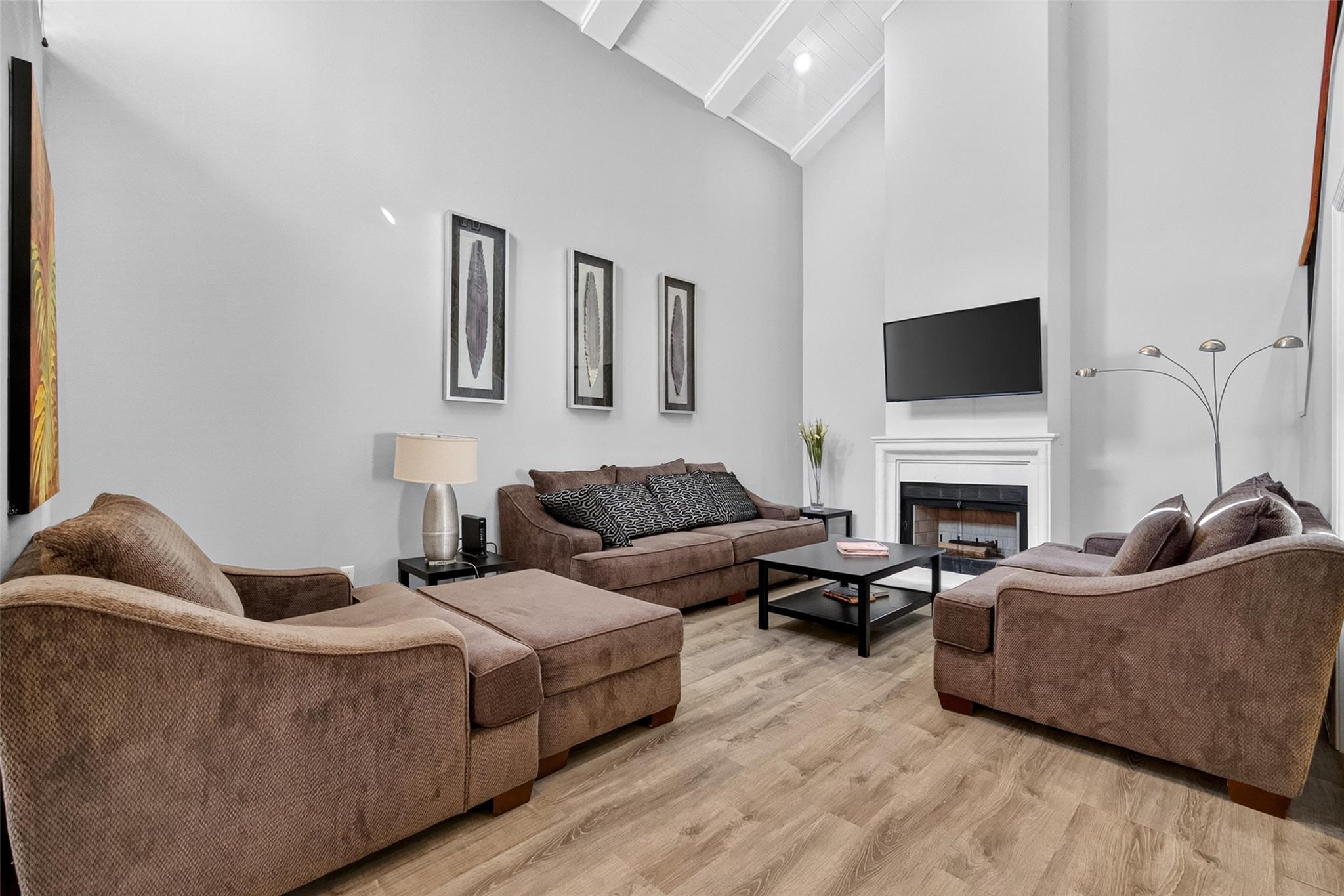 Furnished living room with a vaulted ceiling, brown sectional sofas, and a fireplace beneath a wall-mounted television.