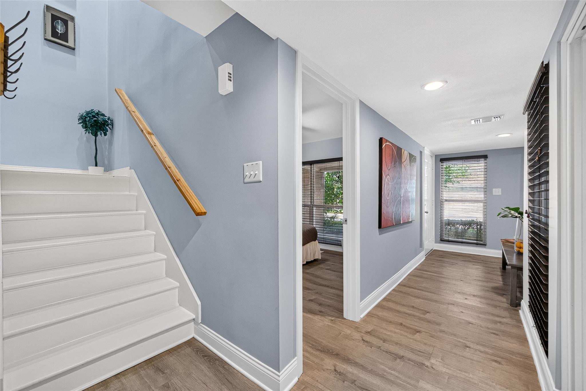 Hallway with white stairs, wood flooring, blue-gray walls, and abstract art.