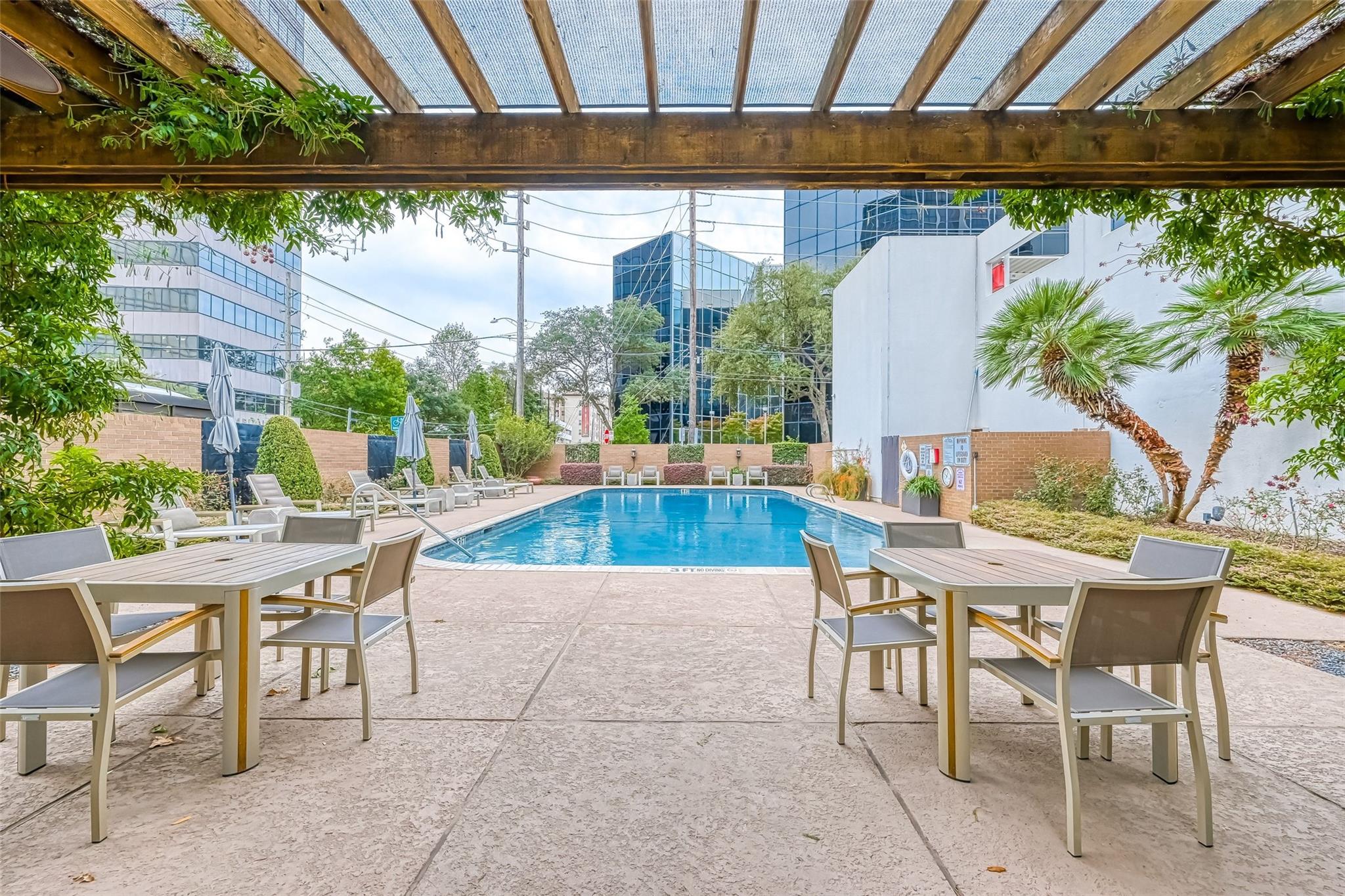 Outdoor pool and patio beneath a wooden pergola, with dining tables and landscaped surroundings.