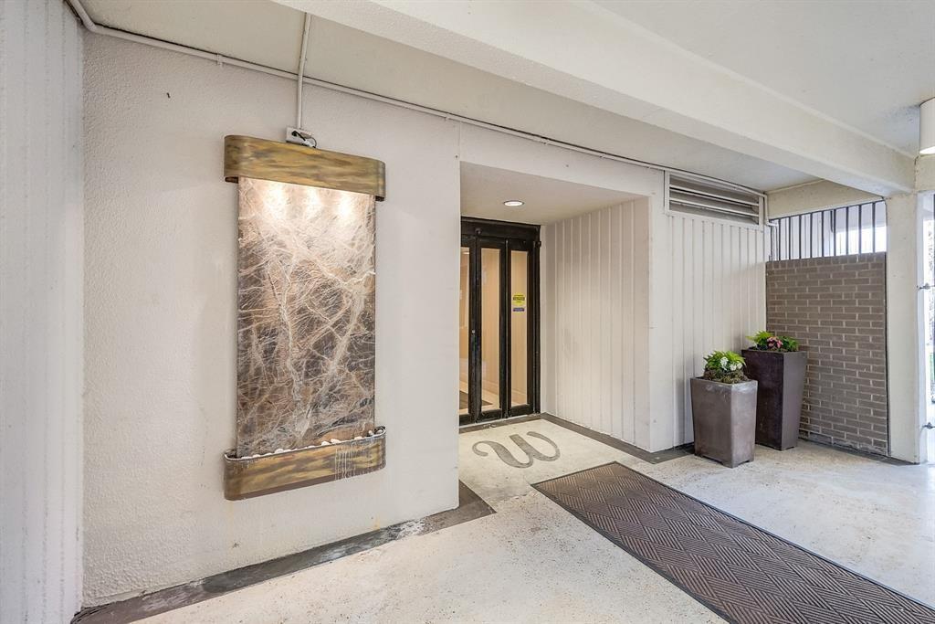 Covered condominium entrance with glass doors, a wall fountain, and potted plants.