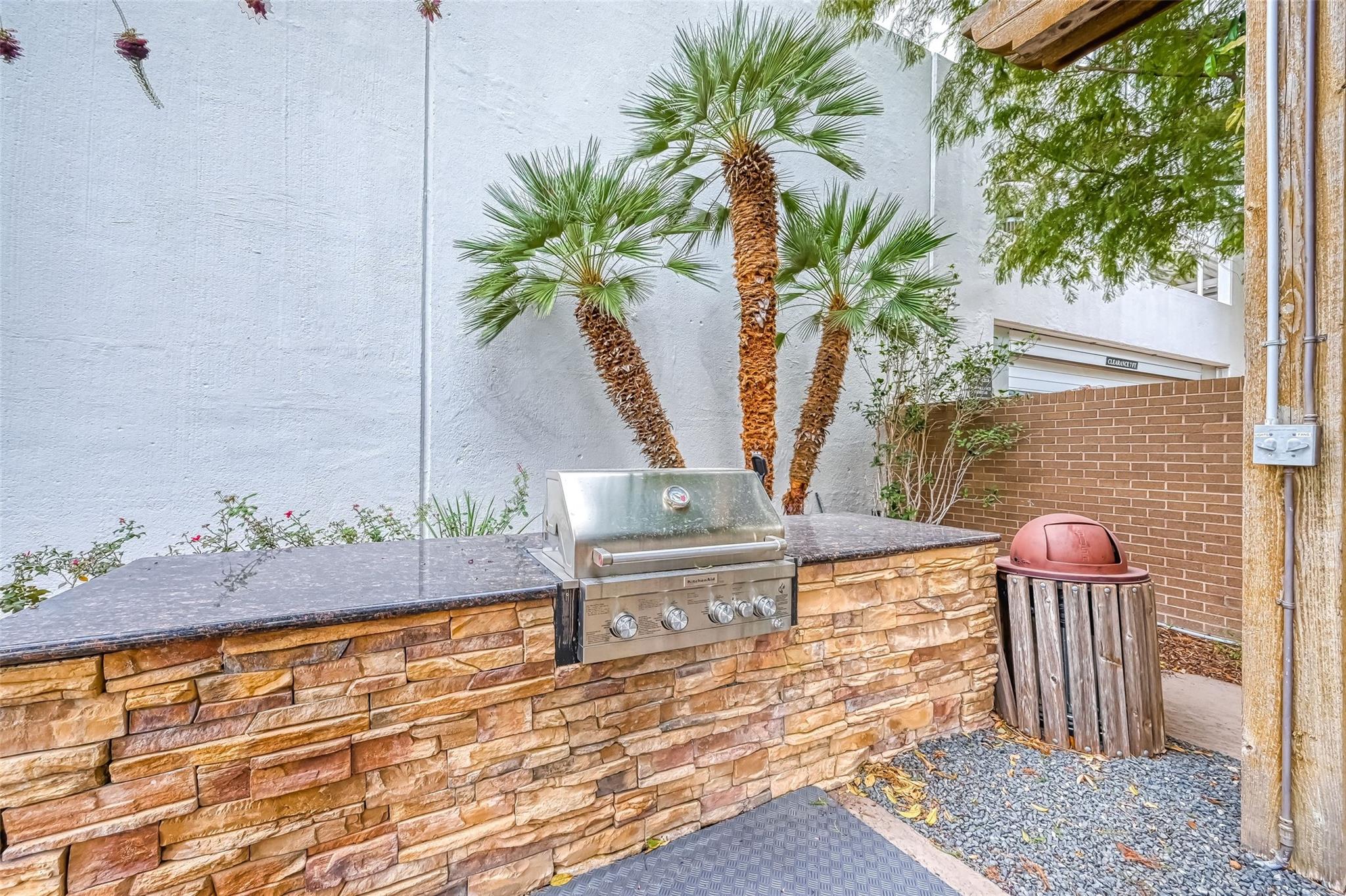 Outdoor grilling area with a built-in stainless-steel grill and stone counter beneath palm trees.