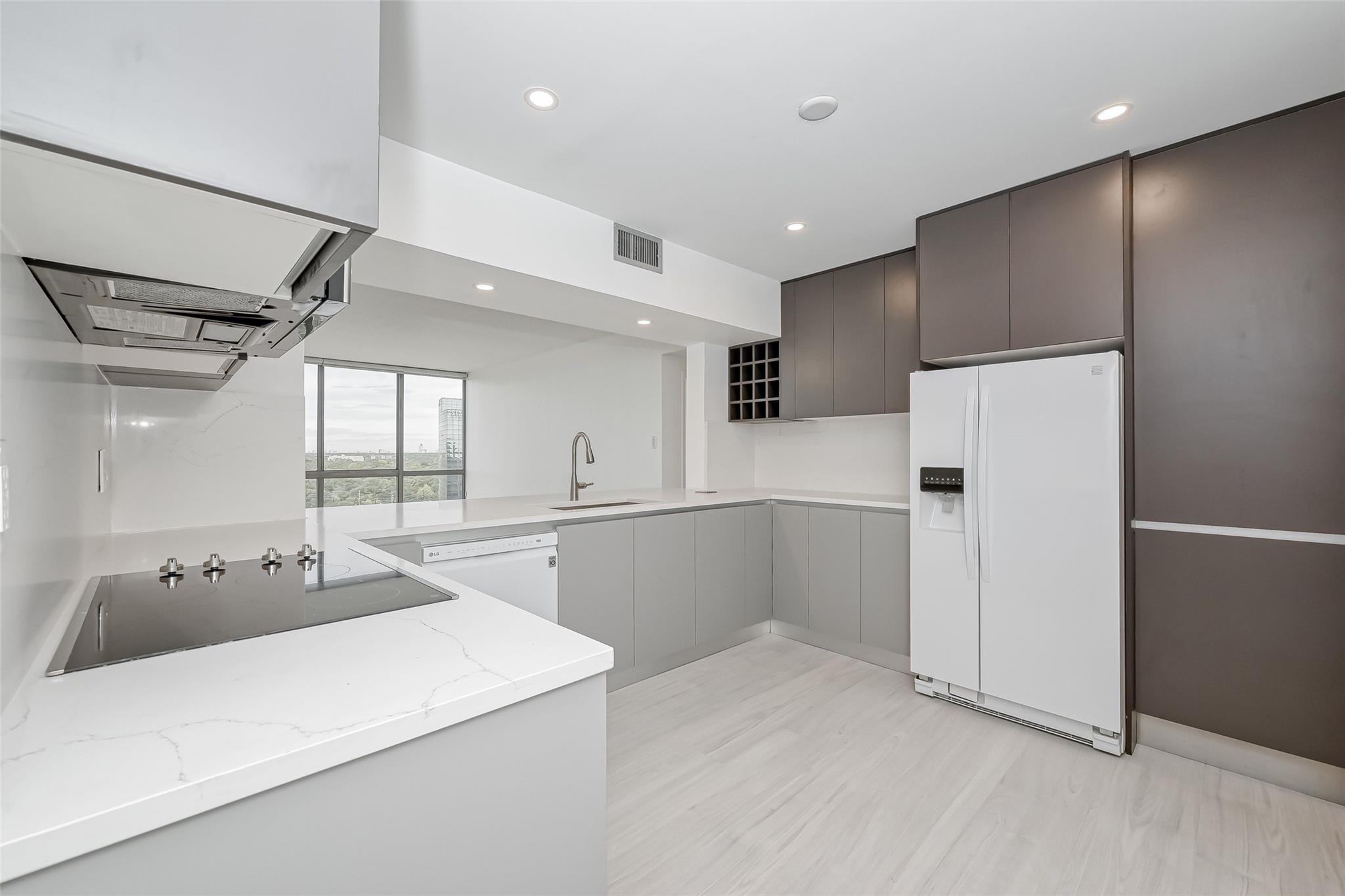 Modern condo kitchen with gray cabinetry, white quartz counters, and a large window overlooking trees.