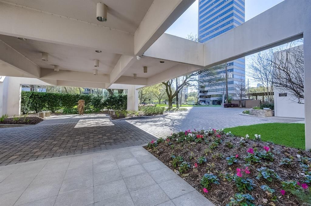 Covered high-rise entrance with a paved drive, landscaped flower beds, and a modern tower beyond.