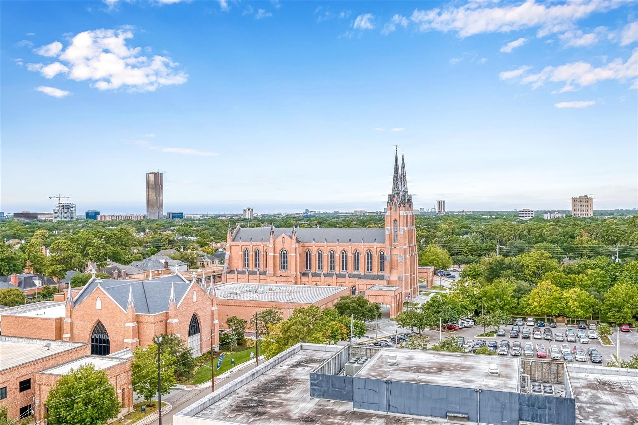Elevated Houston view over leafy neighborhoods, featuring a red-brick church with twin spires.