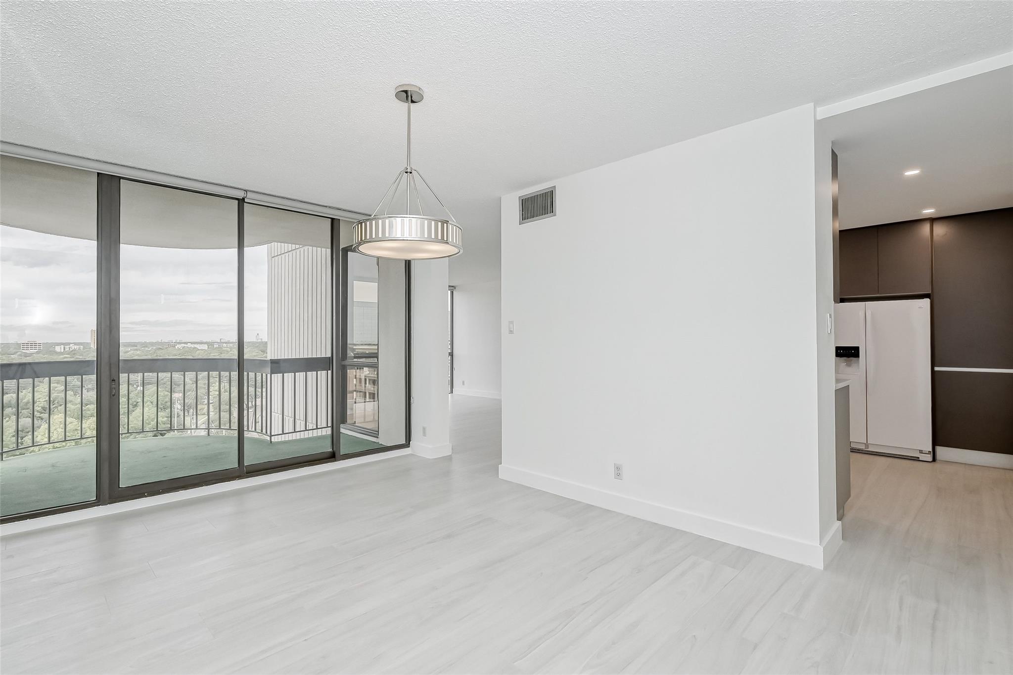 Vacant condo living area with balcony doors, pale flooring, pendant light, and distant views.
