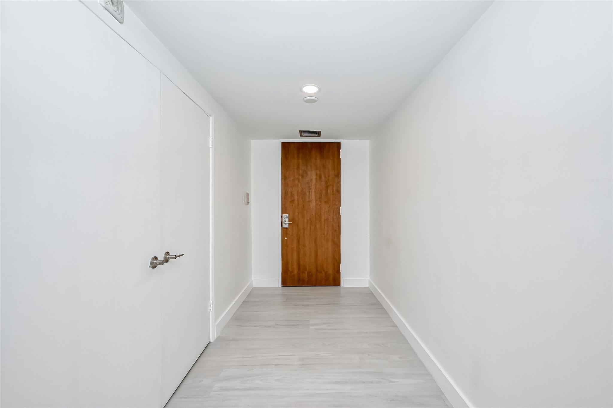 Vacant entry hallway with light gray flooring and a brown wooden door.