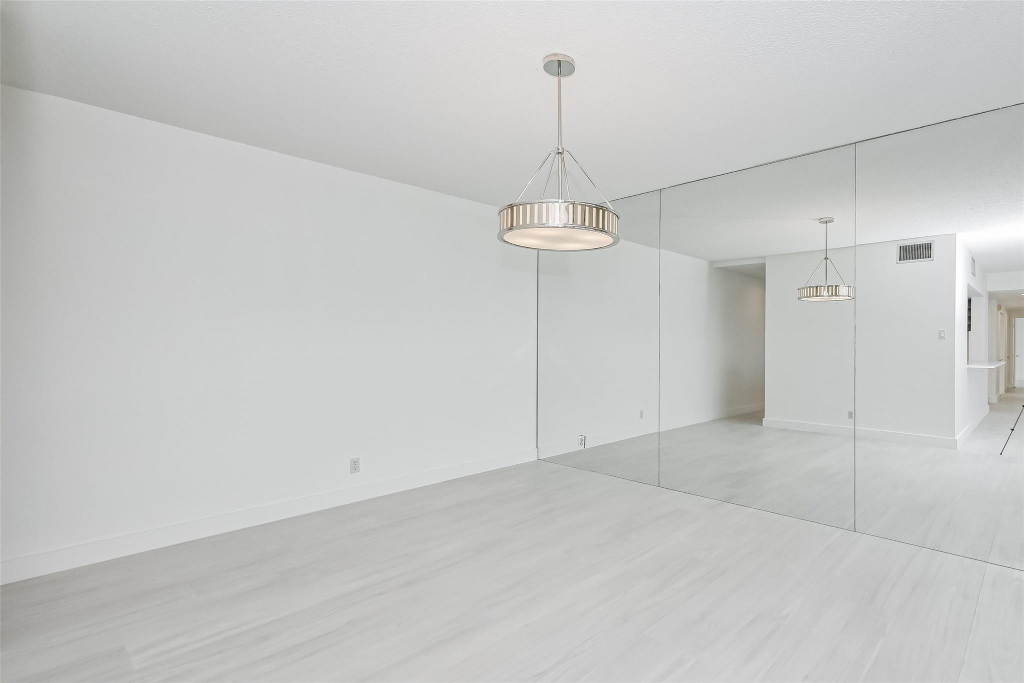 Empty interior room with pale wood floors, a mirrored wall, and a circular pendant light.