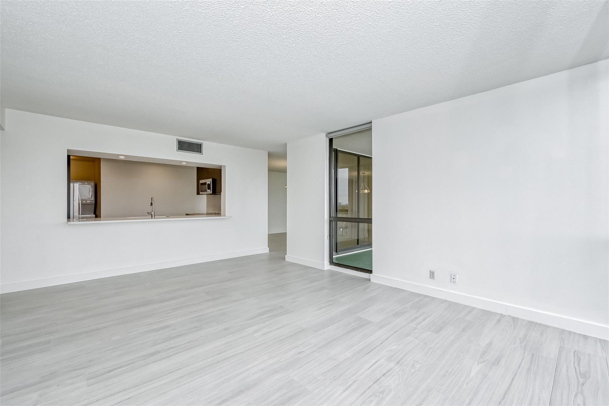 Vacant living room with pale flooring, a kitchen pass-through, and a sliding glass balcony door.