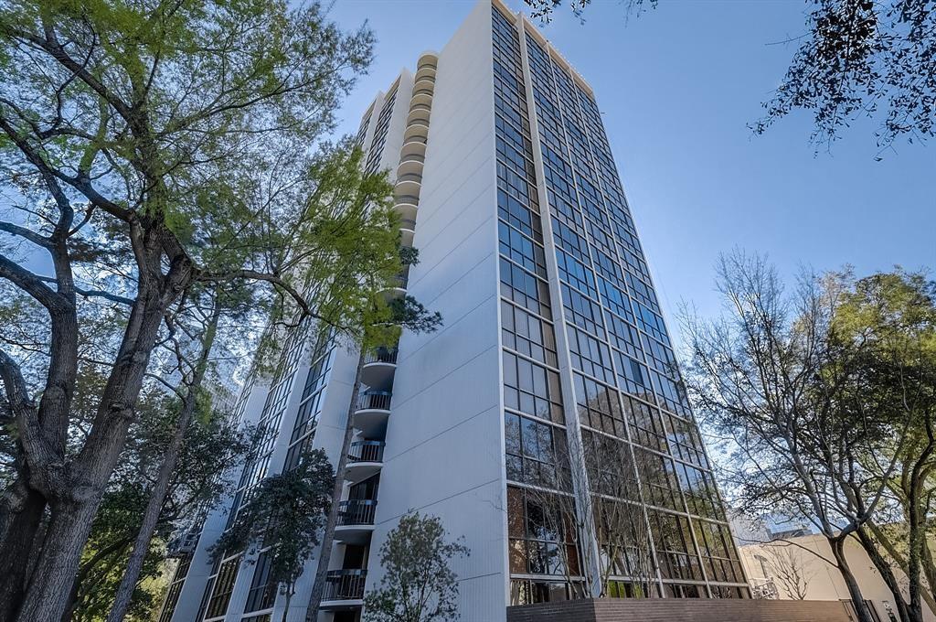 High-rise condominium tower with a white facade, broad glass windows, curved balconies, and mature trees.