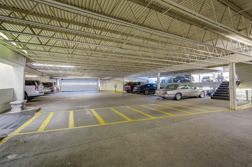 Covered parking garage with yellow-marked spaces, parked cars, exposed roof trusses, and a stairway.