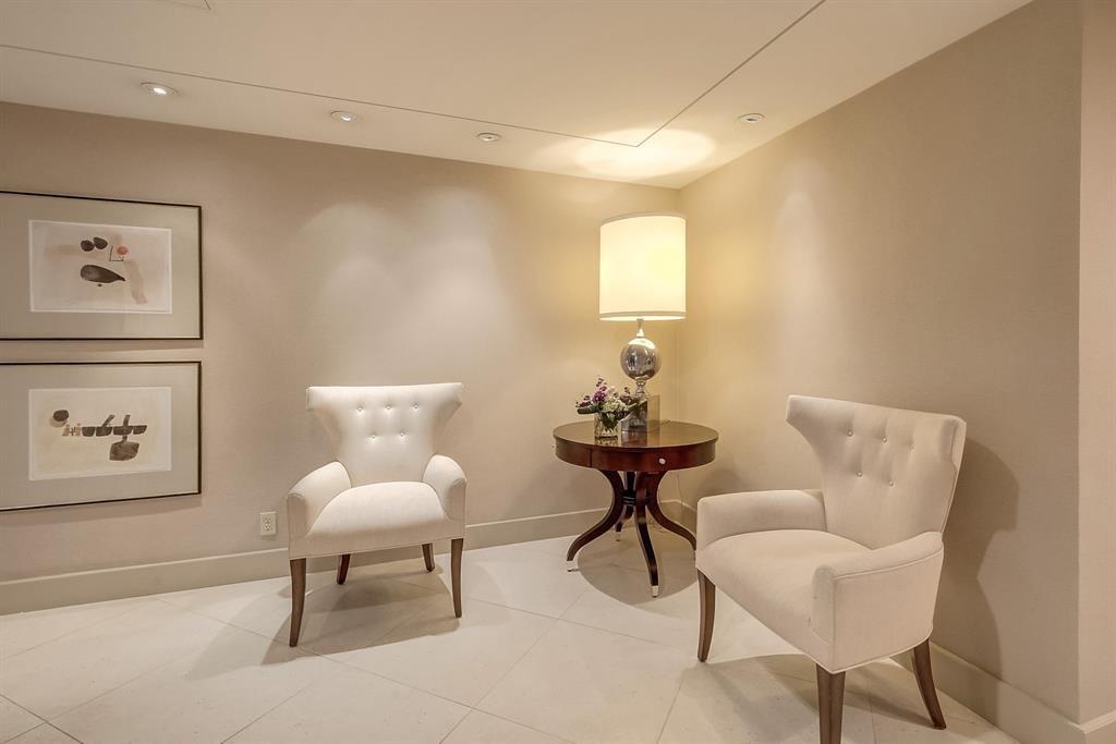 Condominium sitting area with cream armchairs, a round table, and framed abstract art.