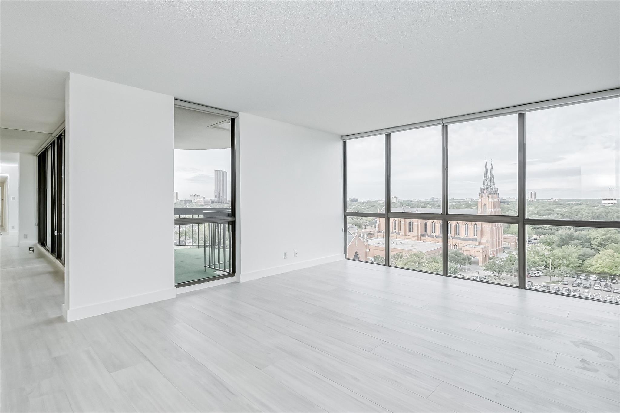 Vacant condo living area with floor-to-ceiling windows overlooking a Gothic church and Houston skyline.