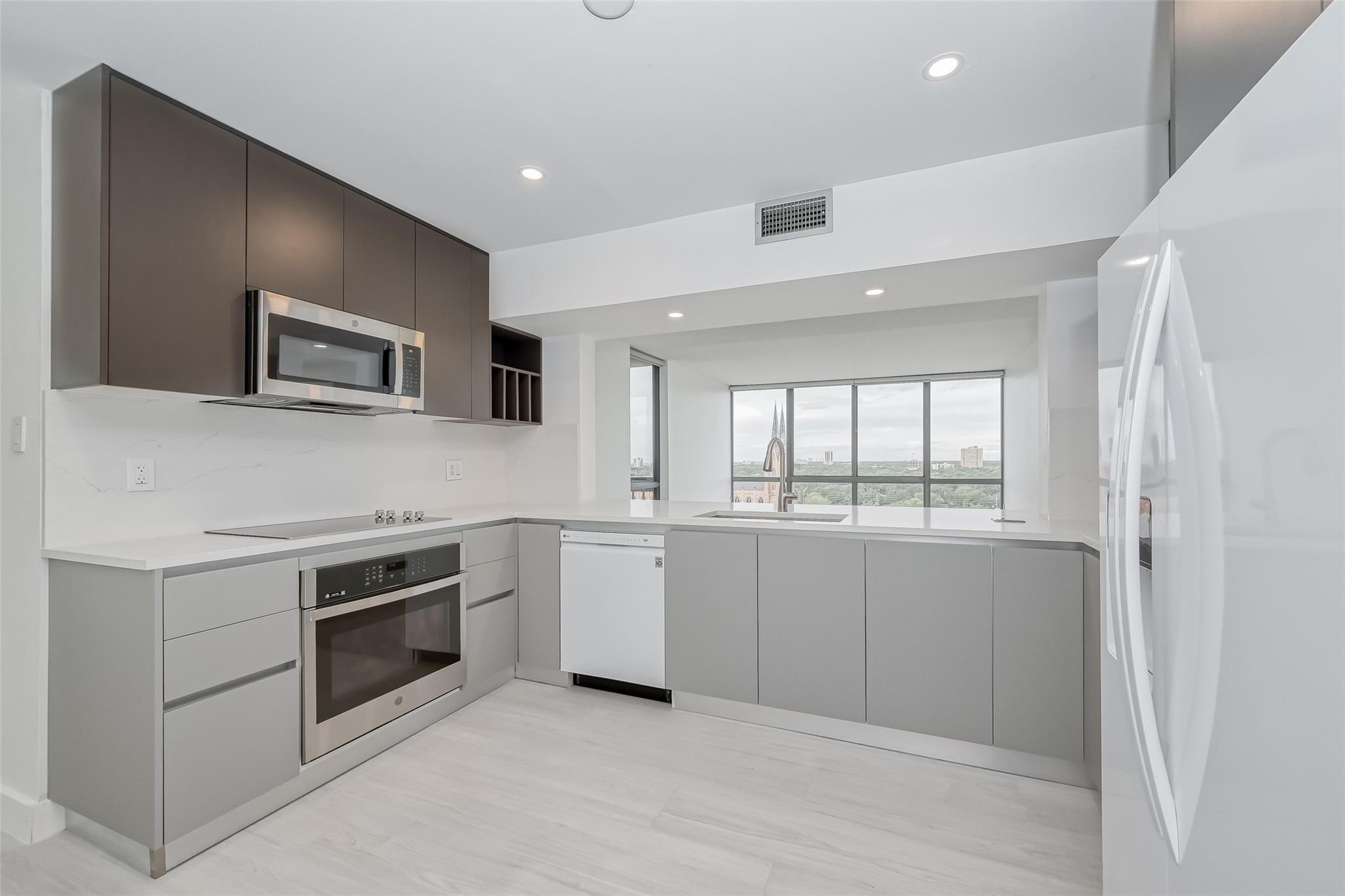 Modern gray-and-white kitchen with stainless steel appliances and a broad window overlooking the city.