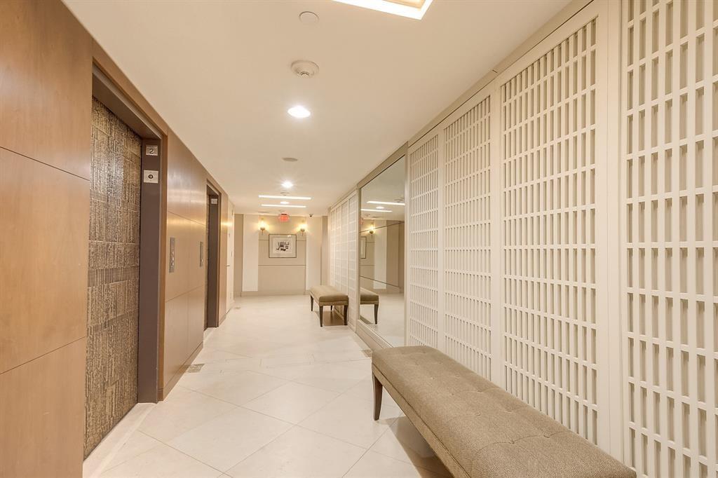 Residential hallway with elevators, upholstered benches, and white lattice walls.
