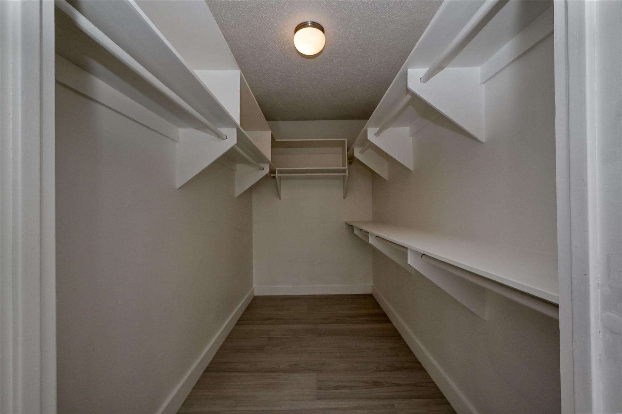 Empty walk-in closet with white shelving and hanging rods on both sides.