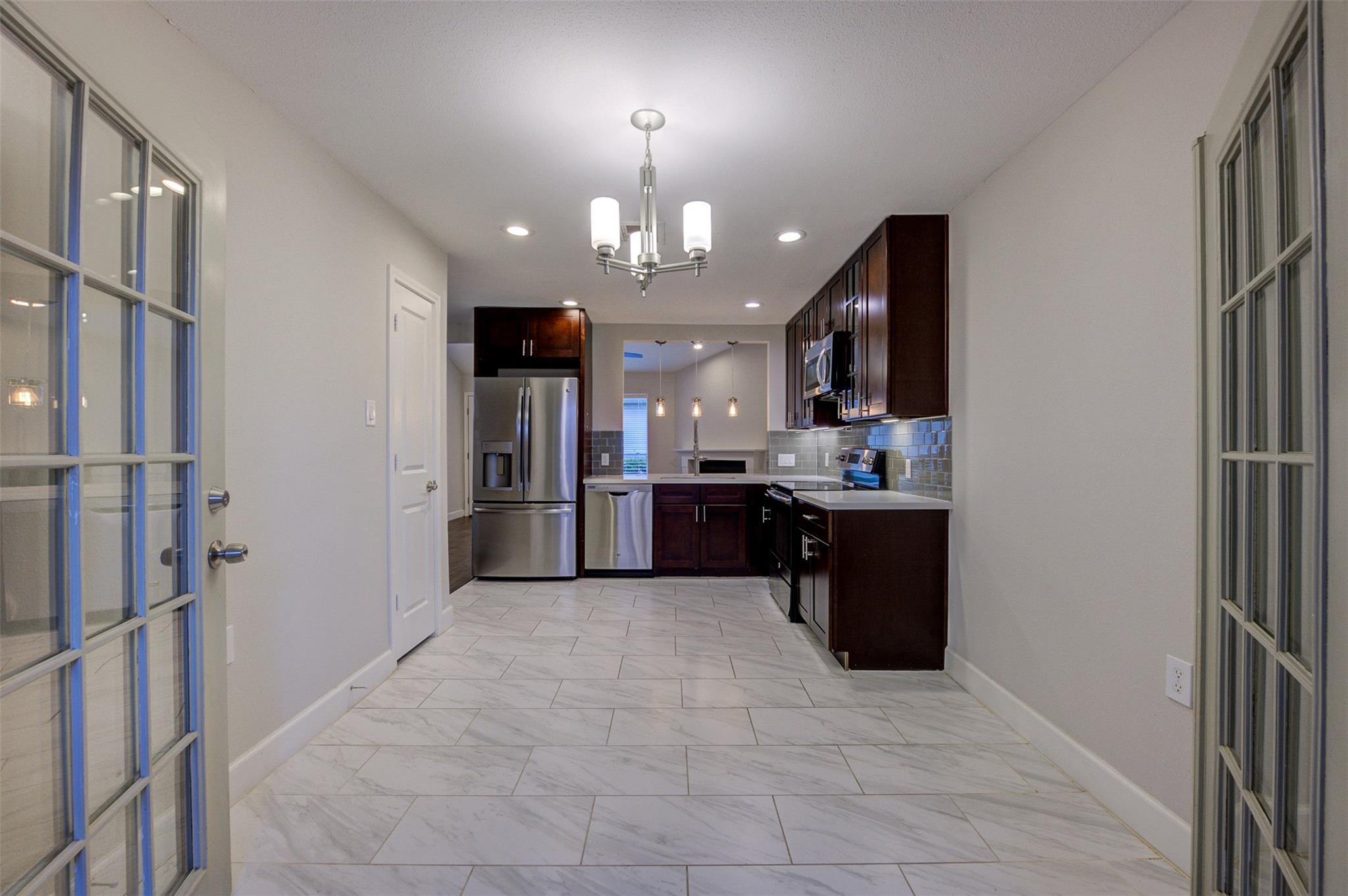 Kitchen with dark wood cabinets, stainless steel appliances, and large light-colored tile floors.