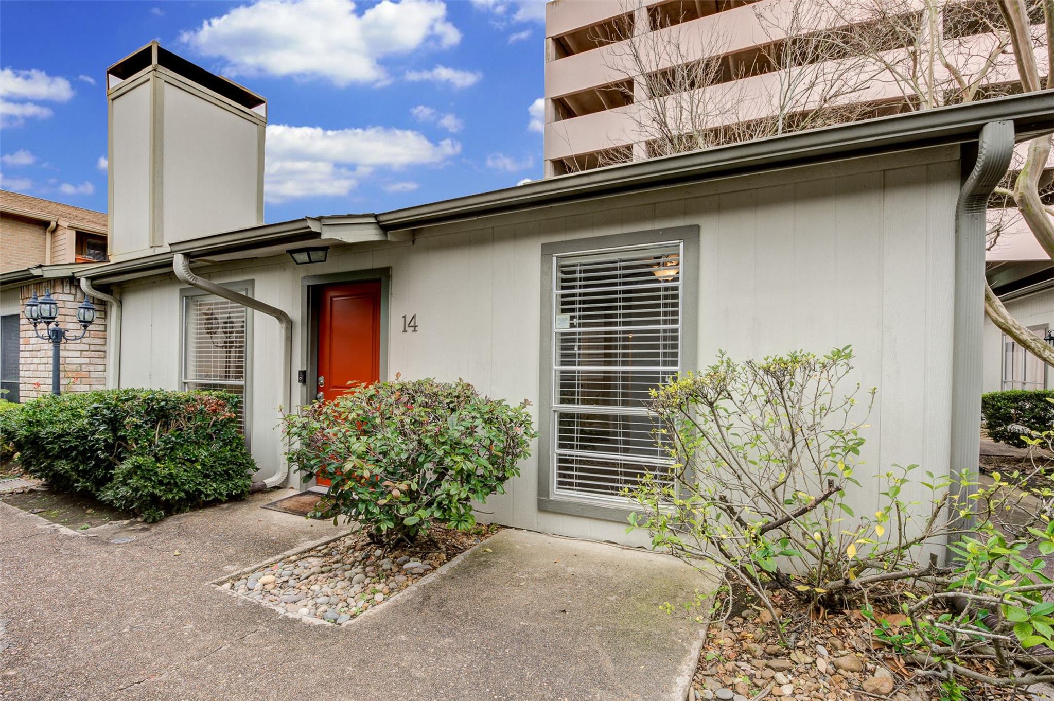 Condominium unit 14 with a red front door, light siding, and shrubs beside the walkway.