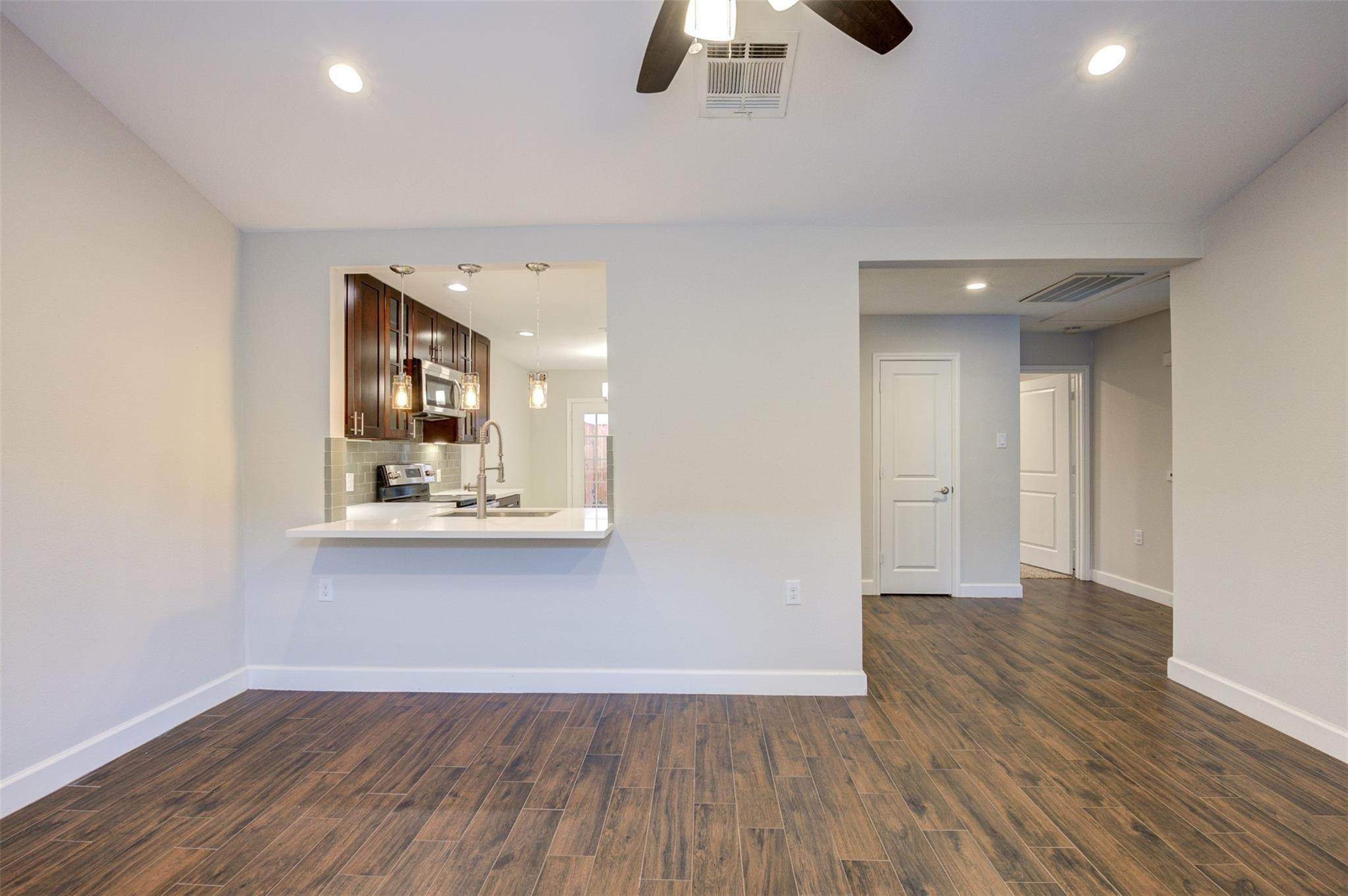 Vacant room with wood-look floors and a breakfast bar opening onto a dark-cabinet kitchen.