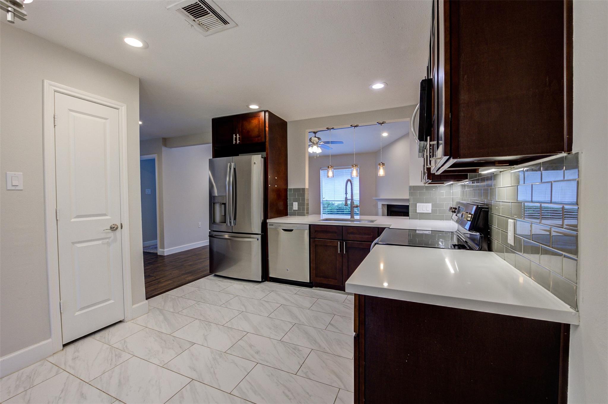 Modern kitchen with dark wood cabinets, stainless steel appliances, and marble-look tile flooring.