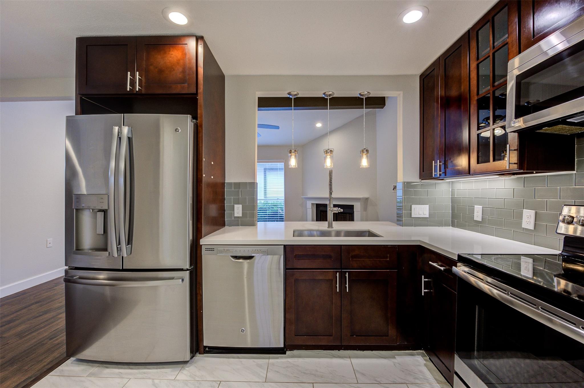 Kitchen with dark wood cabinets, stainless steel appliances, and a sink beneath three pendant lights.