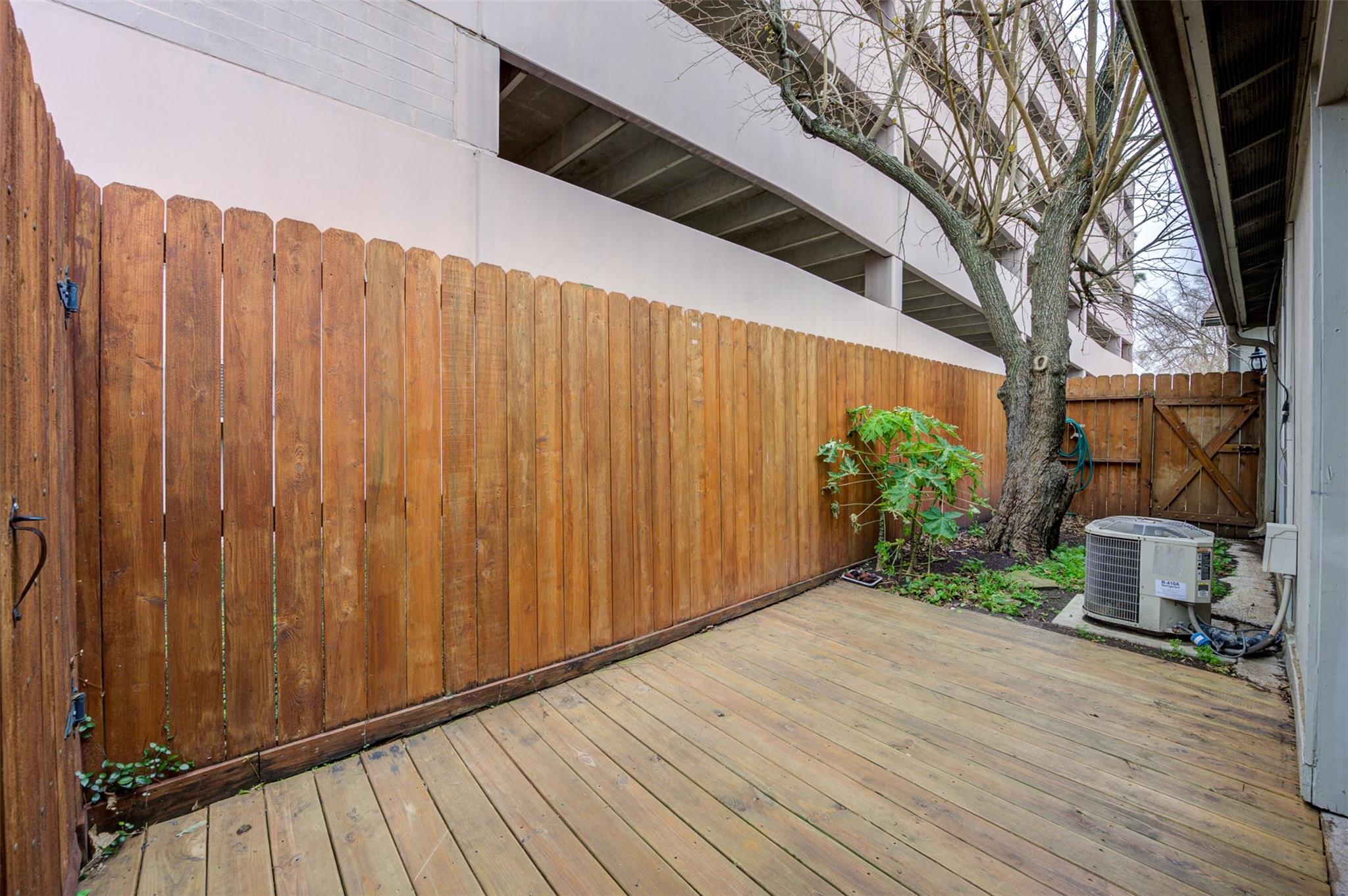 Private wooden deck patio with a tall privacy fence and mature tree.